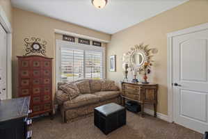 Carpeted room featuring a window with white plantation shutters, a white paneled door with black hardware, and light beige wall paint