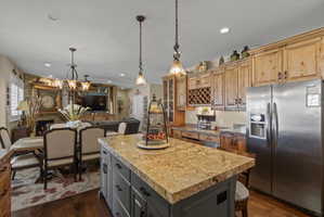 Spacious kitchen featuring a large island with a stone-finish countertop, stainless steel refrigerator, wood-finish cabinetry, and built-in wine storage
