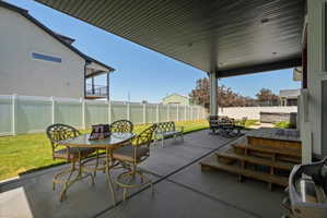 Covered patio featuring concrete flooring, a white vinyl fence, and a manicured lawn