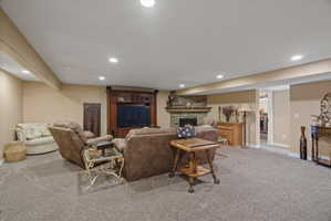 Carpeted recreation room featuring a stone-front fireplace with a wood mantle, recessed lighting, a built-in entertainment center, and neutral paint tones