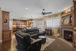 Open-concept living space featuring wood-finish flooring, a stone-faced fireplace with a wood mantle, recessed lighting, and a ceiling fan