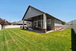 Expansive green lawn with a covered patio, featuring a vinyl privacy fence, stone accent pillars, and a mountain backdrop