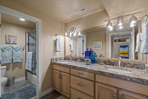 Bathroom featuring a dual-sink vanity with a light-toned countertop, wood-finish cabinetry, and a large wall-mounted mirror