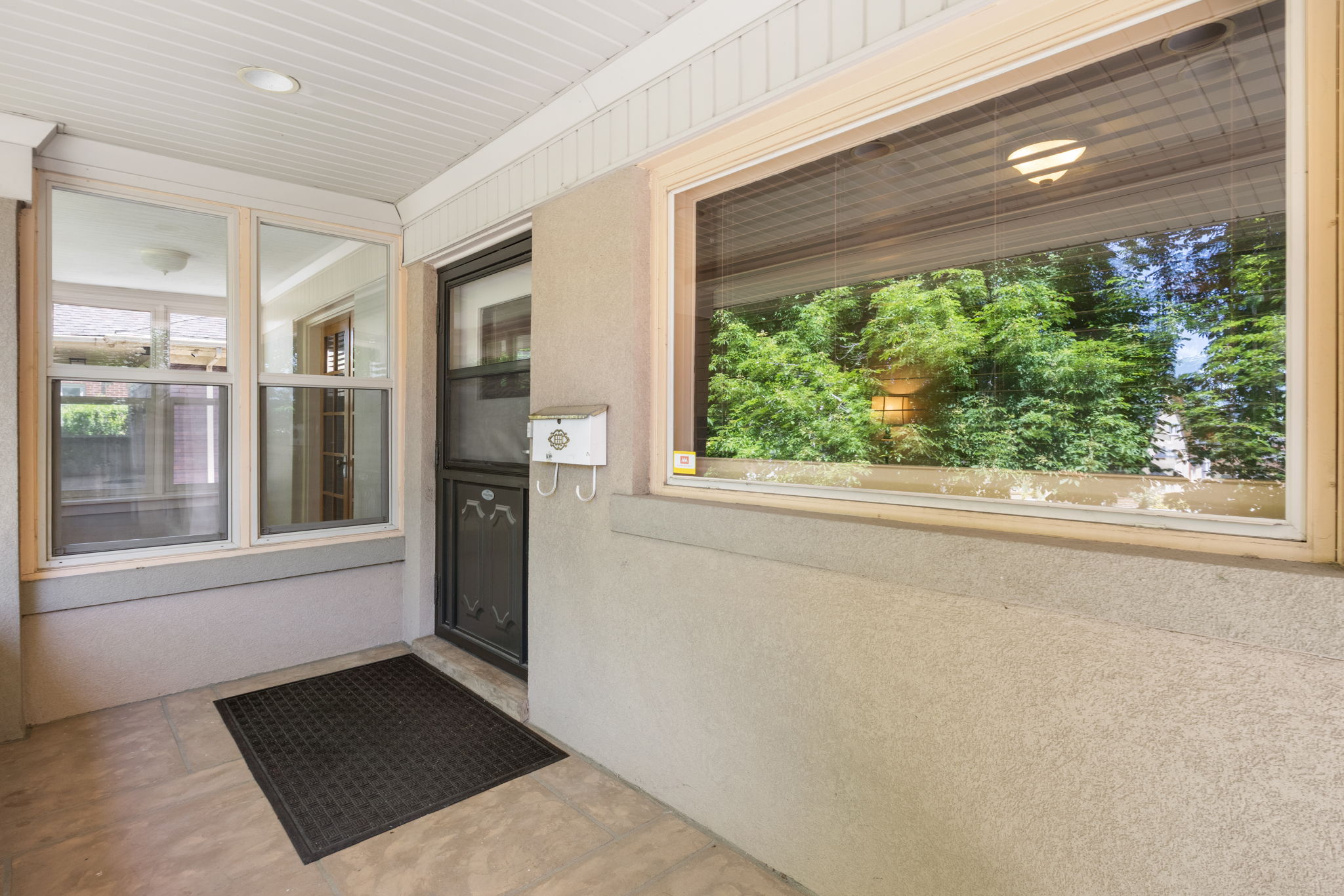 Covered porch entry featuring a dark-framed screen door, a recessed ceiling light, and a horizontal window with a green outdoor backdrop