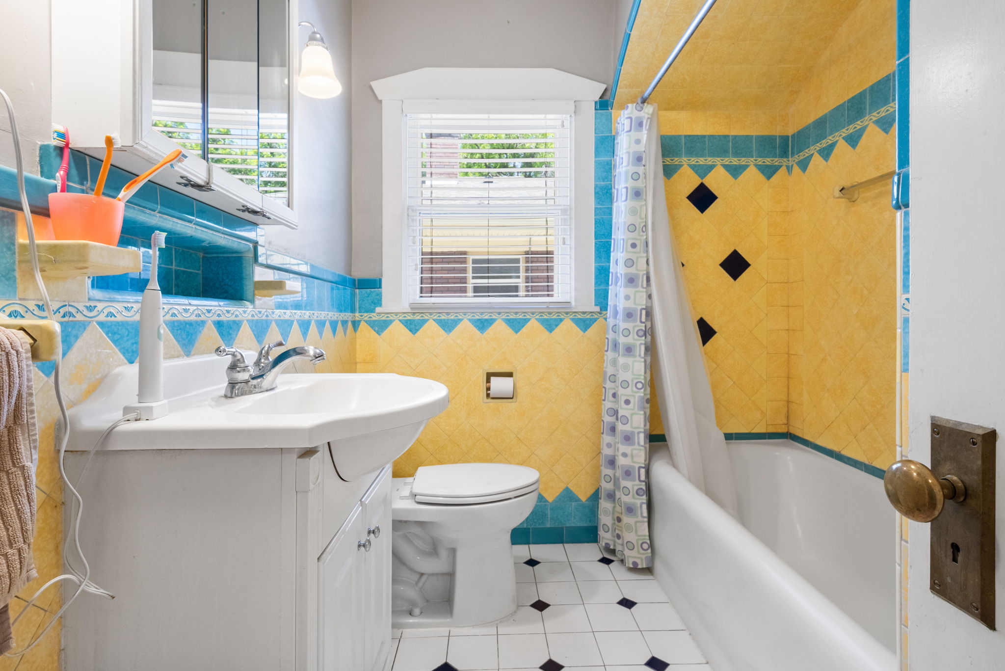 Bathroom featuring pedestal sink, white toilet, and a combination tub and shower with yellow and blue wall tile