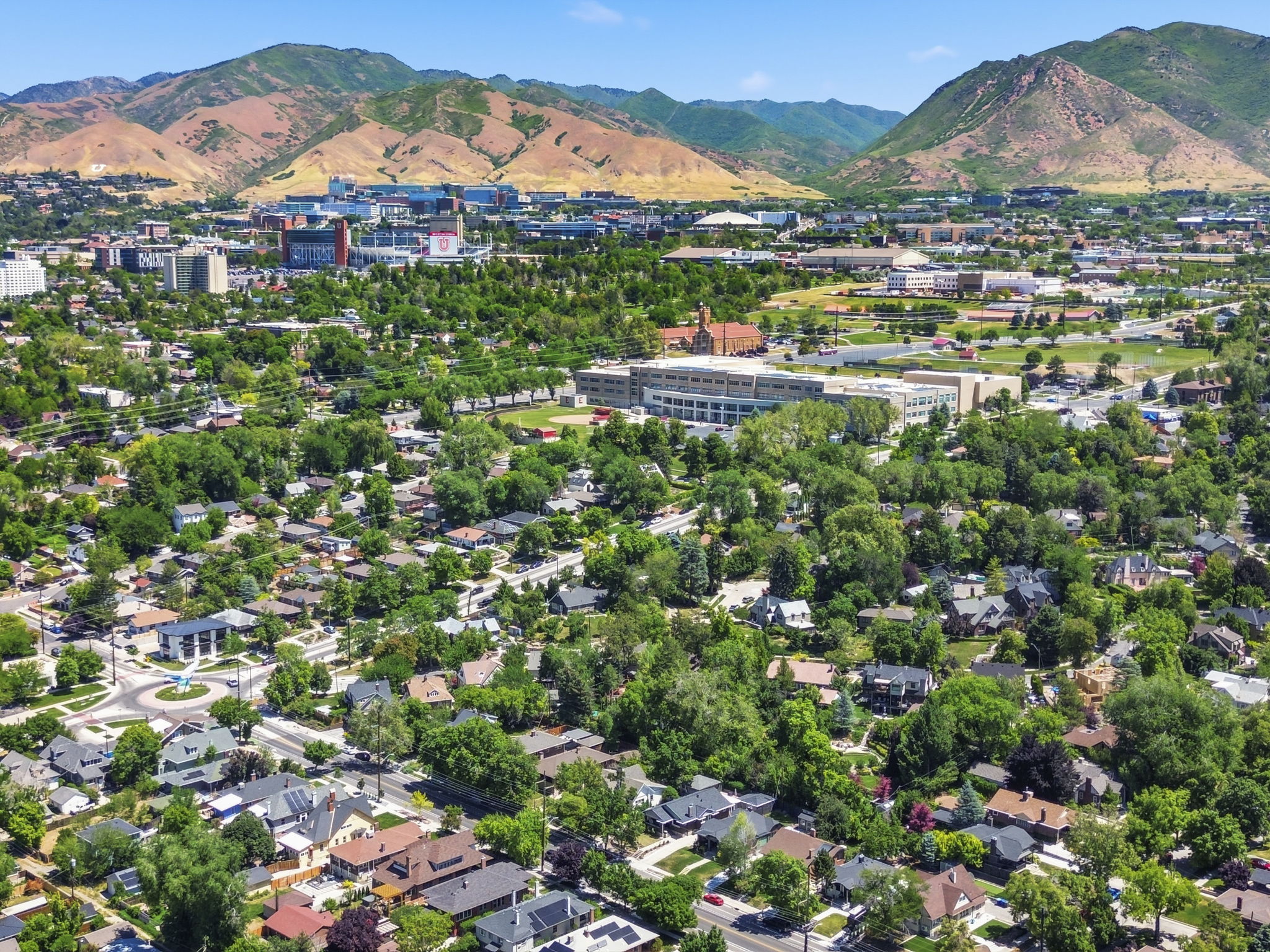 Expansive aerial landscape highlighting a residential neighborhood with established trees, framed by distant mountains