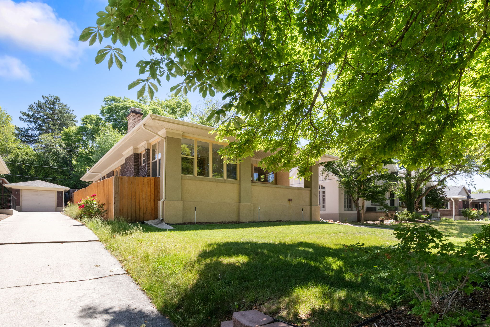 Mature tree canopies shade a verdant lawn, framing a stucco exterior with a prominent window bank