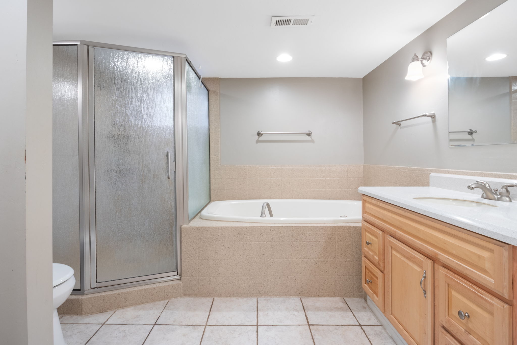 Bathroom featuring a glass-enclosed shower, a built-in soaking tub with a tiled surround, a light wood-finish vanity with a white countertop and integrated sink, and white square floor tiles