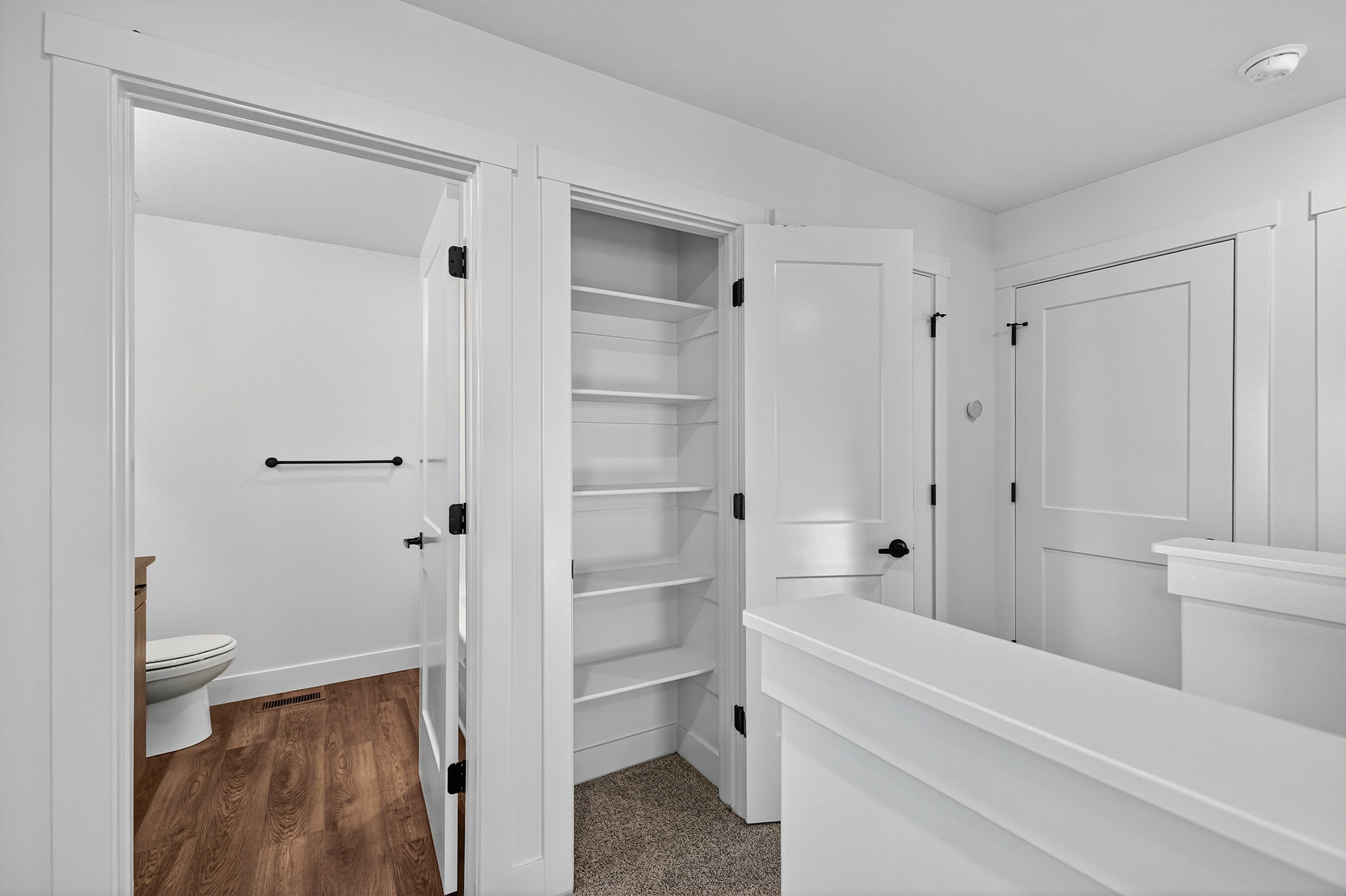 Functional hallway featuring a built-in linen closet with shelving, bright white trim, and a contemporary railing