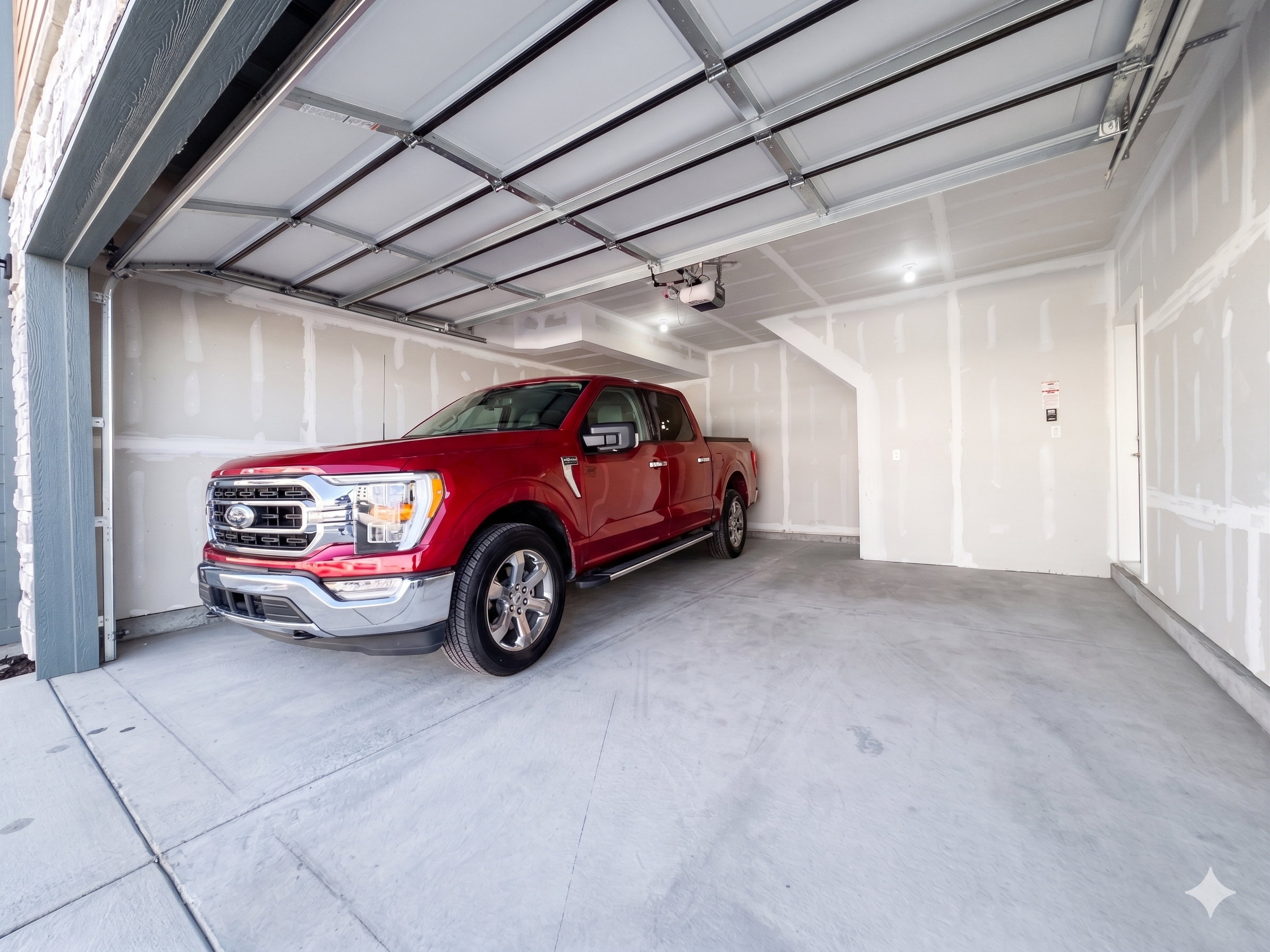 Spacious garage featuring a concrete floor, overhead lighting, an automatic garage door opener, and unfinished drywall