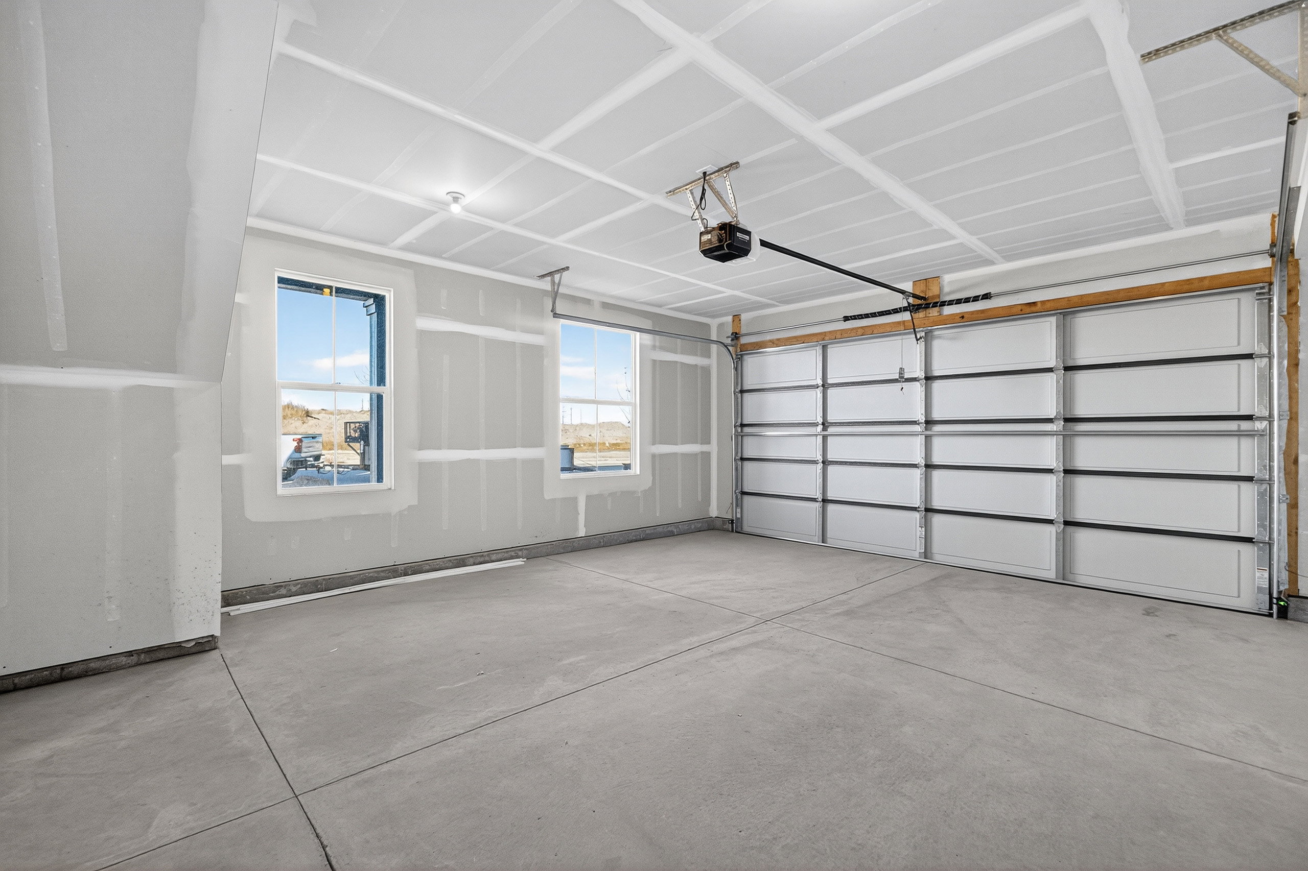 Spacious garage featuring a concrete floor, two windows, and an overhead door with an automatic opener