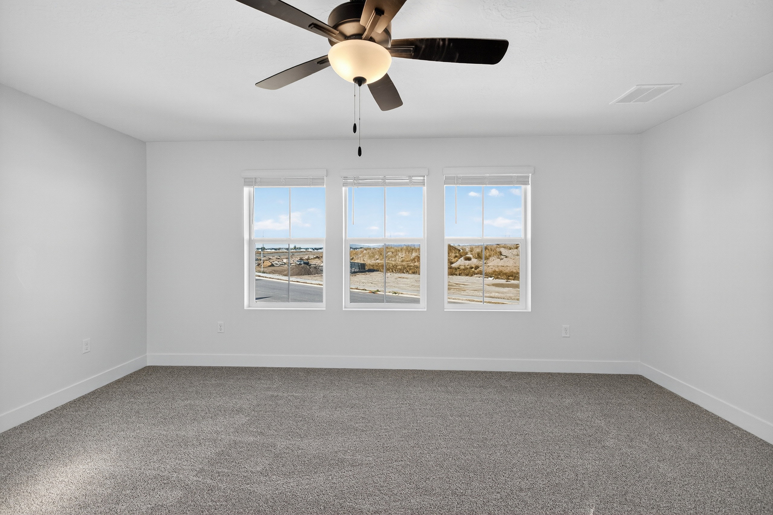 Spacious room featuring three large windows, neutral gray carpeting, white baseboards, and a contemporary ceiling fan with integrated lighting