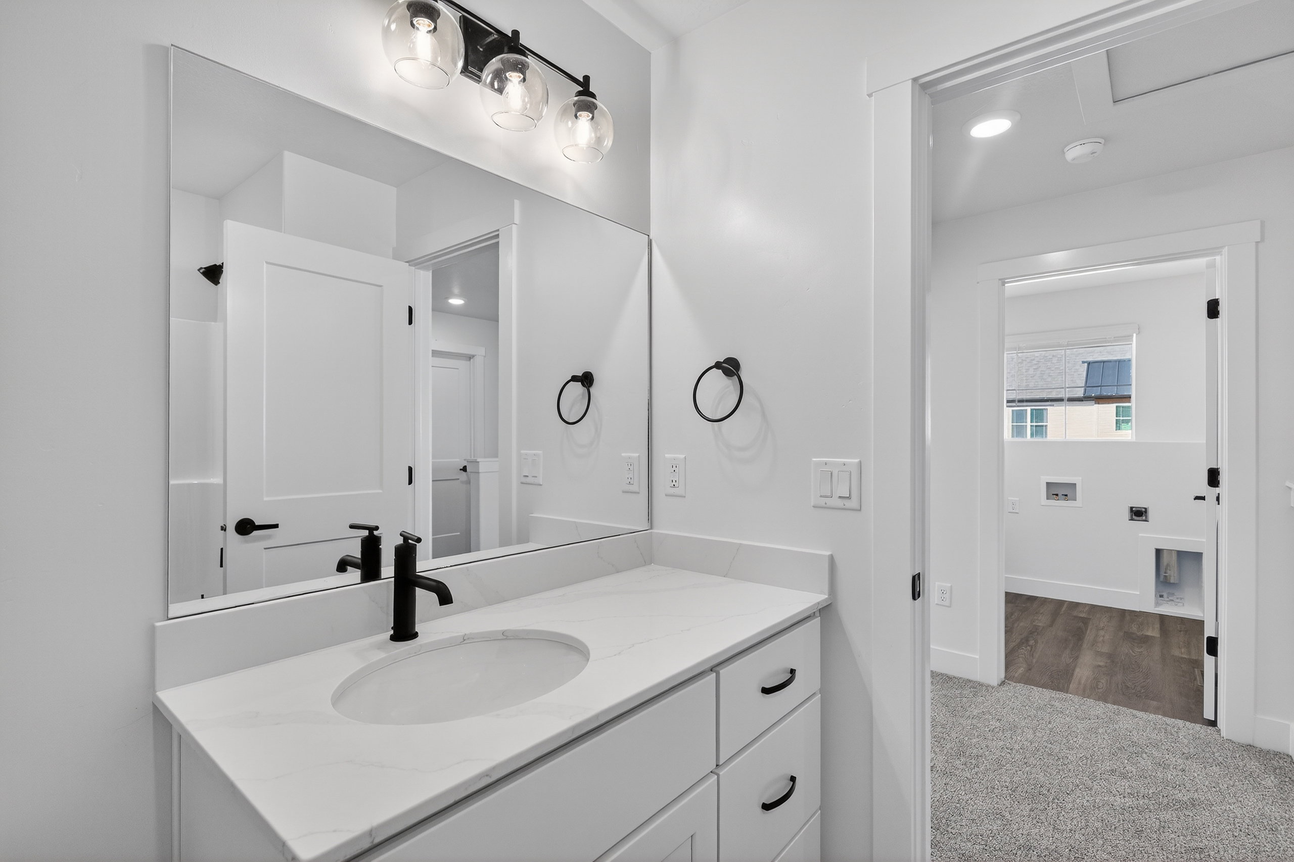 Bathroom vanity featuring a single basin, white countertop, matte black faucet, and a large wall-mounted mirror