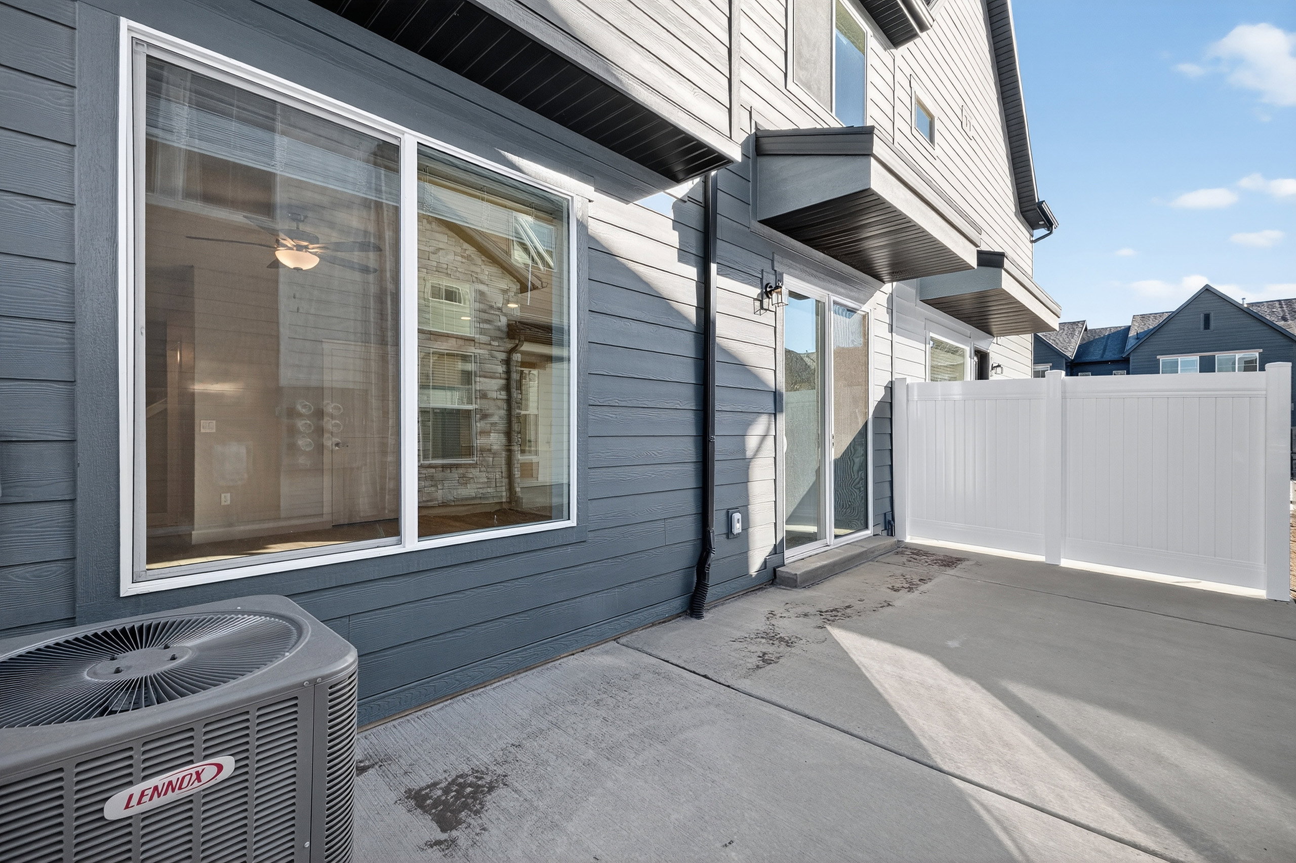 Private concrete patio area featuring a white vinyl fence, sliding glass door access, and large windows