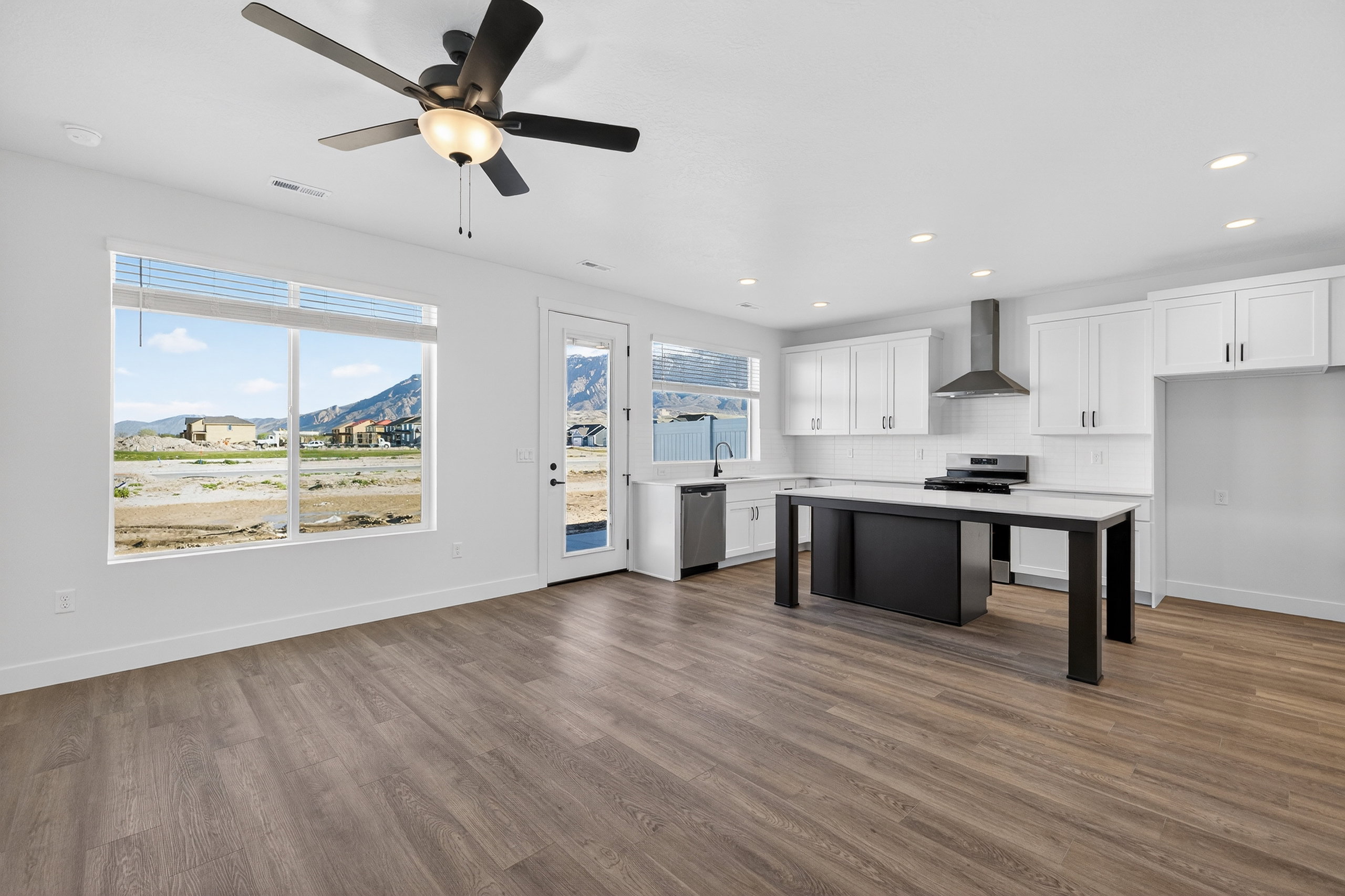Open-concept living area with wood-finish flooring, a contemporary kitchen, white cabinetry, a large kitchen island, and stainless steel appliances