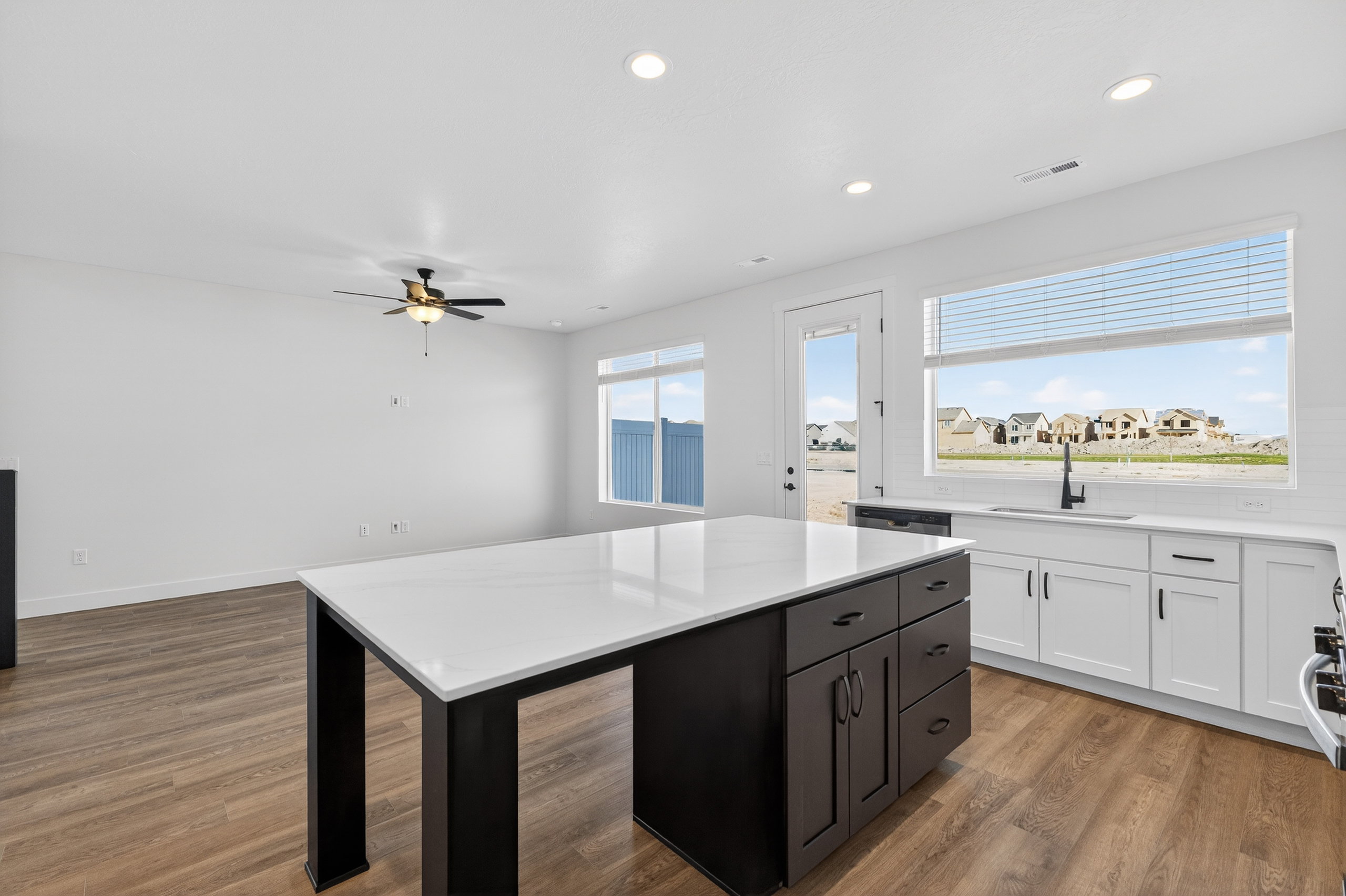 Kitchen featuring a central island with a white countertop and dark cabinetry, white perimeter cabinetry with a white countertop, a stainless steel sink with a matte black faucet, and wood-finish flooring