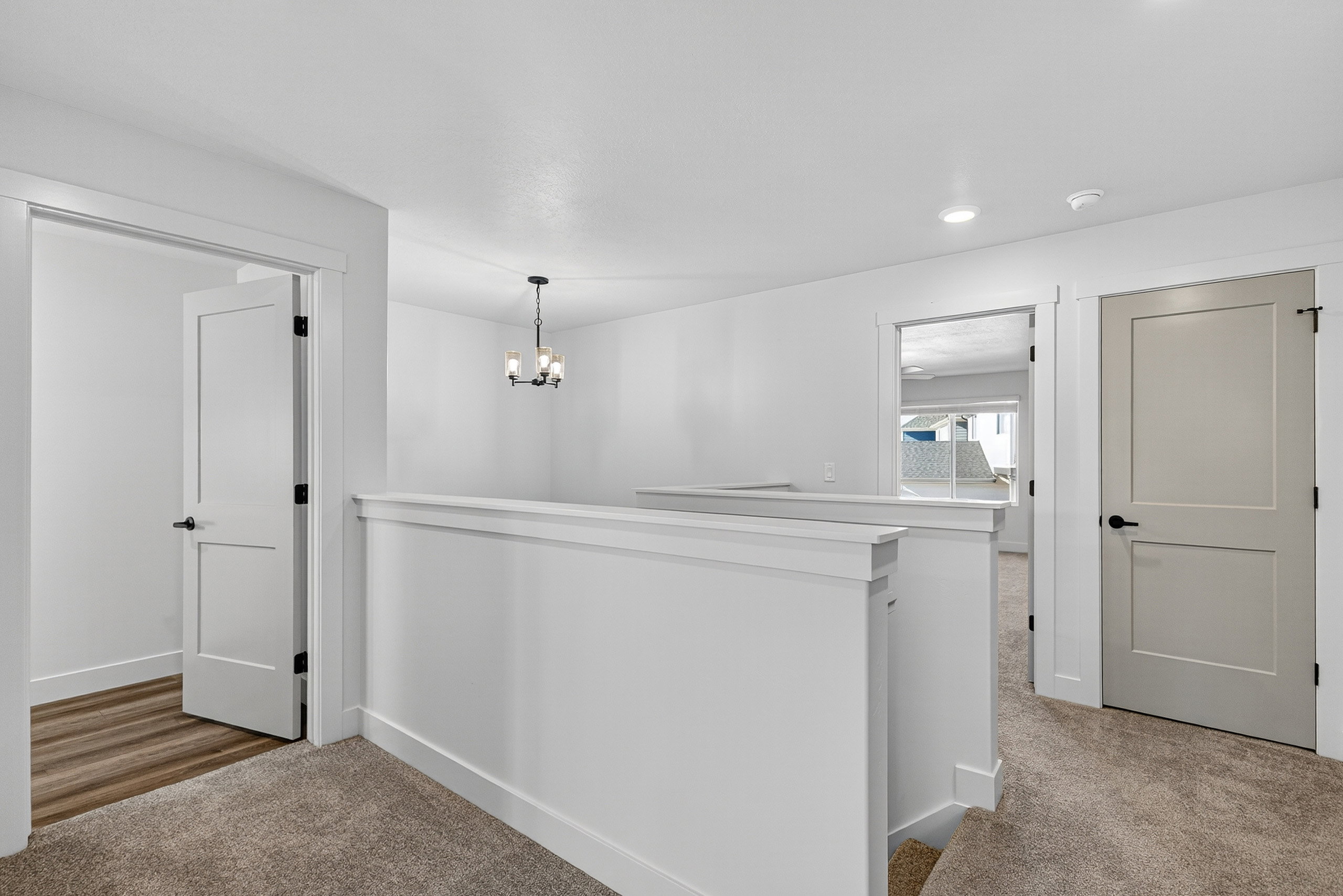 Upper-level landing featuring neutral carpeting, white balustrade, recessed lighting, and a modern chandelier