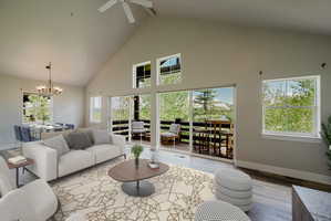 Spacious living area featuring a vaulted ceiling with a ceiling fan, abundant natural light from multiple windows and sliding glass doors, and light wood-finish flooring