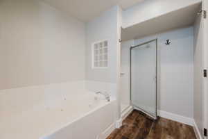 Bathroom featuring a white jetted soaking tub, glass block accent window, walk-in shower with frosted glass door, and wood-finish flooring