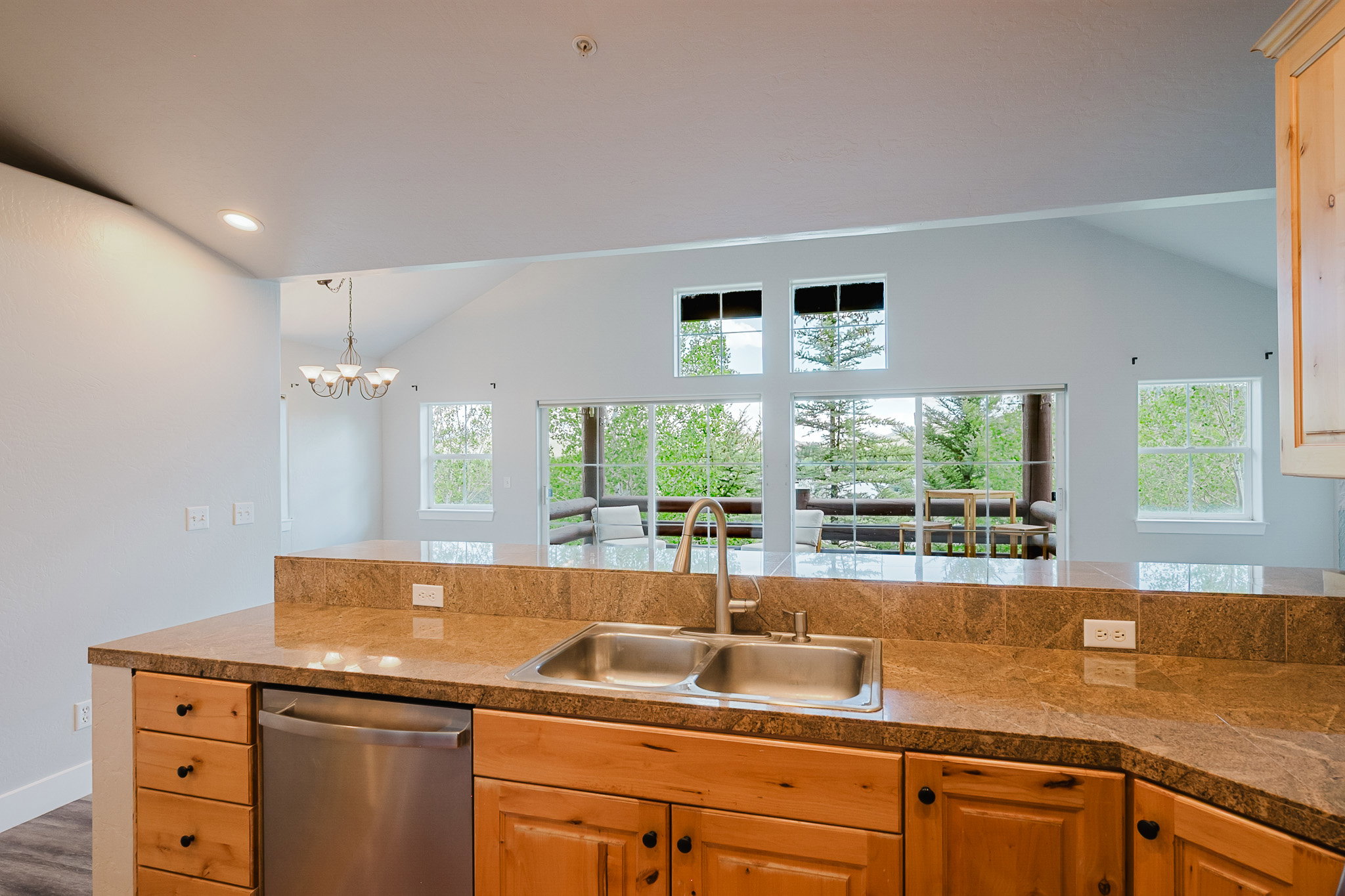 Kitchen featuring granite-style countertops, stainless steel sink with gooseneck faucet, light wood cabinetry with dark hardware, and a stainless steel dishwasher