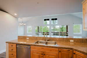 Kitchen featuring granite-style countertops, stainless steel sink with gooseneck faucet, light wood cabinetry with dark hardware, and a stainless steel dishwasher