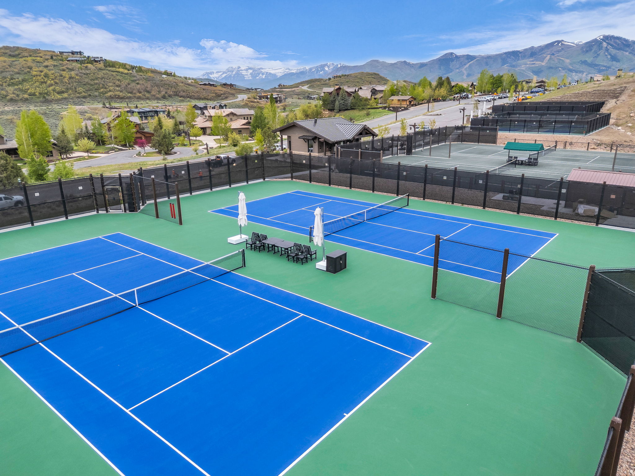 Tennis court complex featuring blue and green hard courts, perimeter fencing, and seating areas
