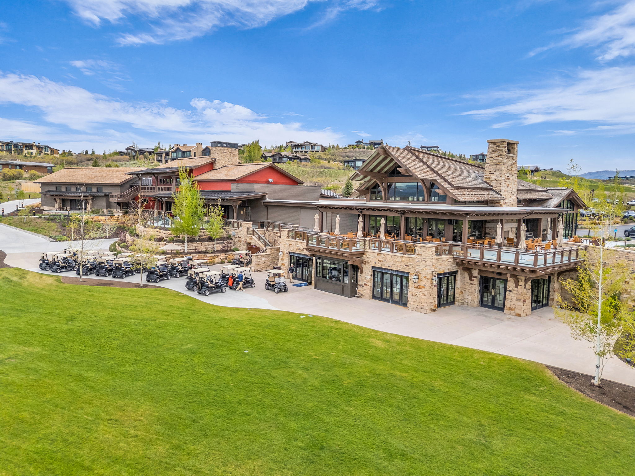 Expansive clubhouse with stone and wood siding, featuring multiple balconies, a prominent stone chimney, and a large manicured lawn