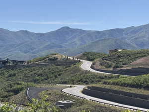 Winding asphalt road with tiered stone retaining walls, surrounded by verdant hillsides and distant mountains