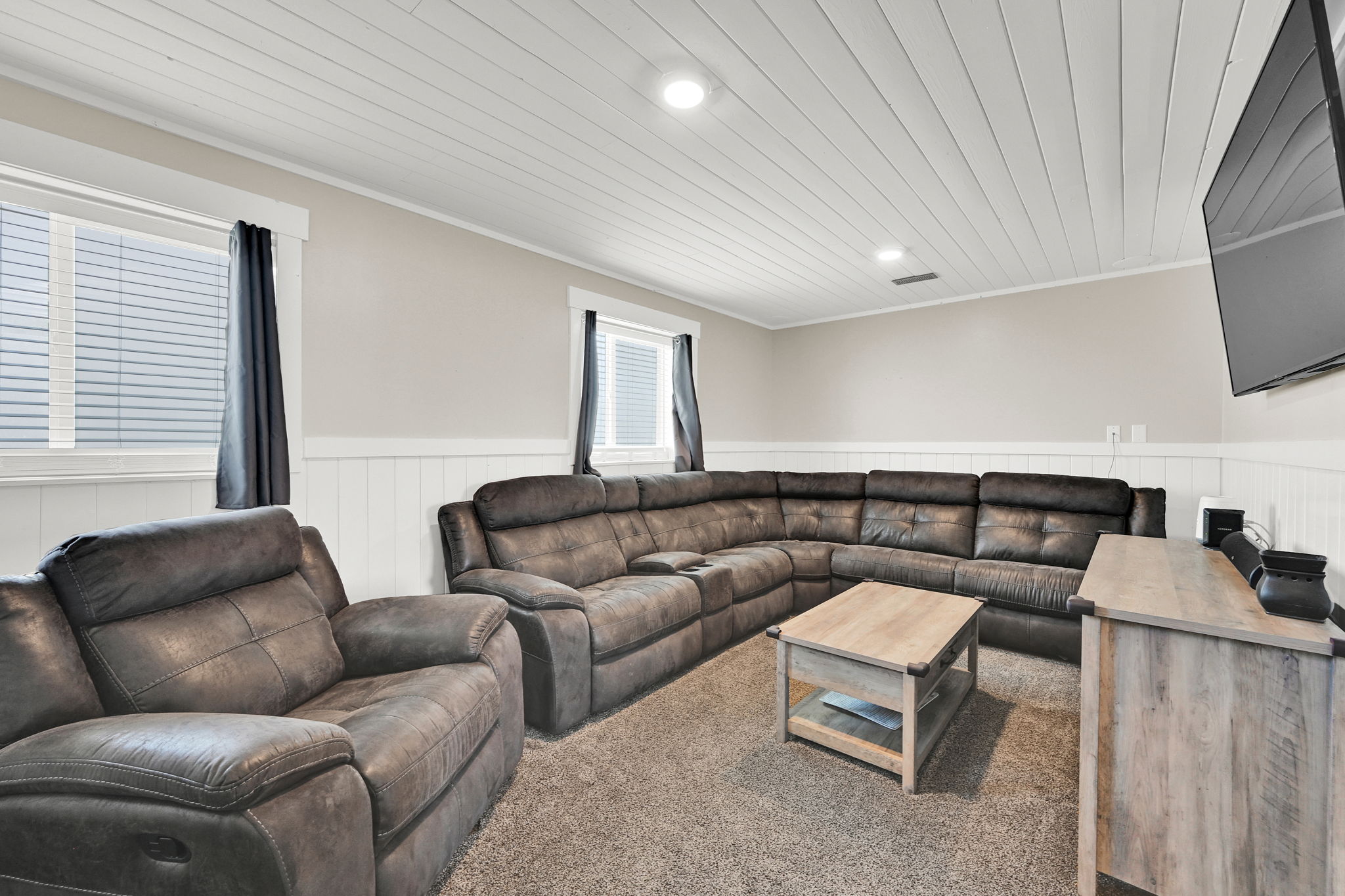 Spacious living area featuring neutral-toned walls, white beadboard wainscoting, and a paneled ceiling with recessed lighting