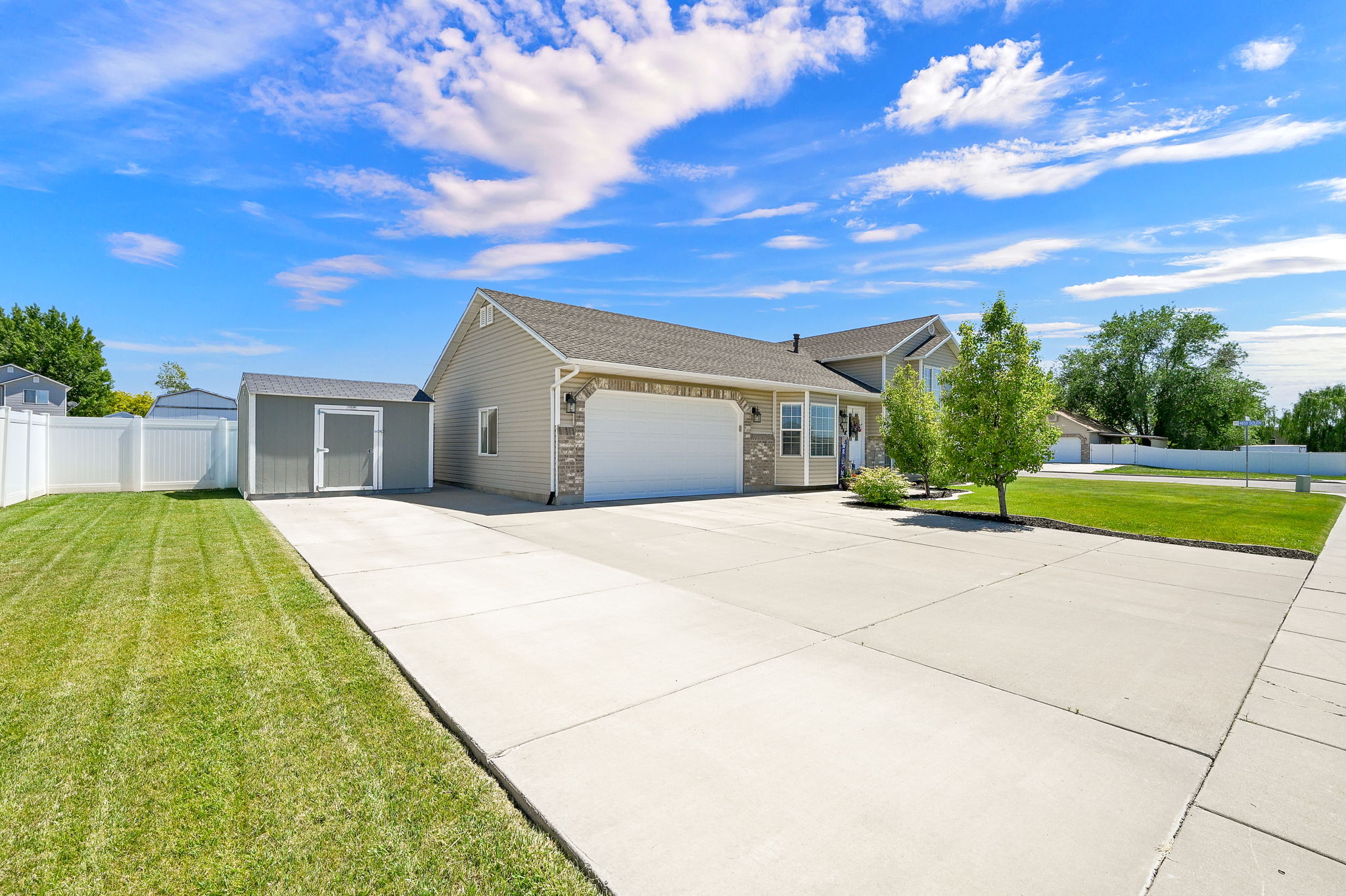 Spacious concrete driveway featuring a two-car garage, established front yard landscaping, and a side yard with a storage shed
