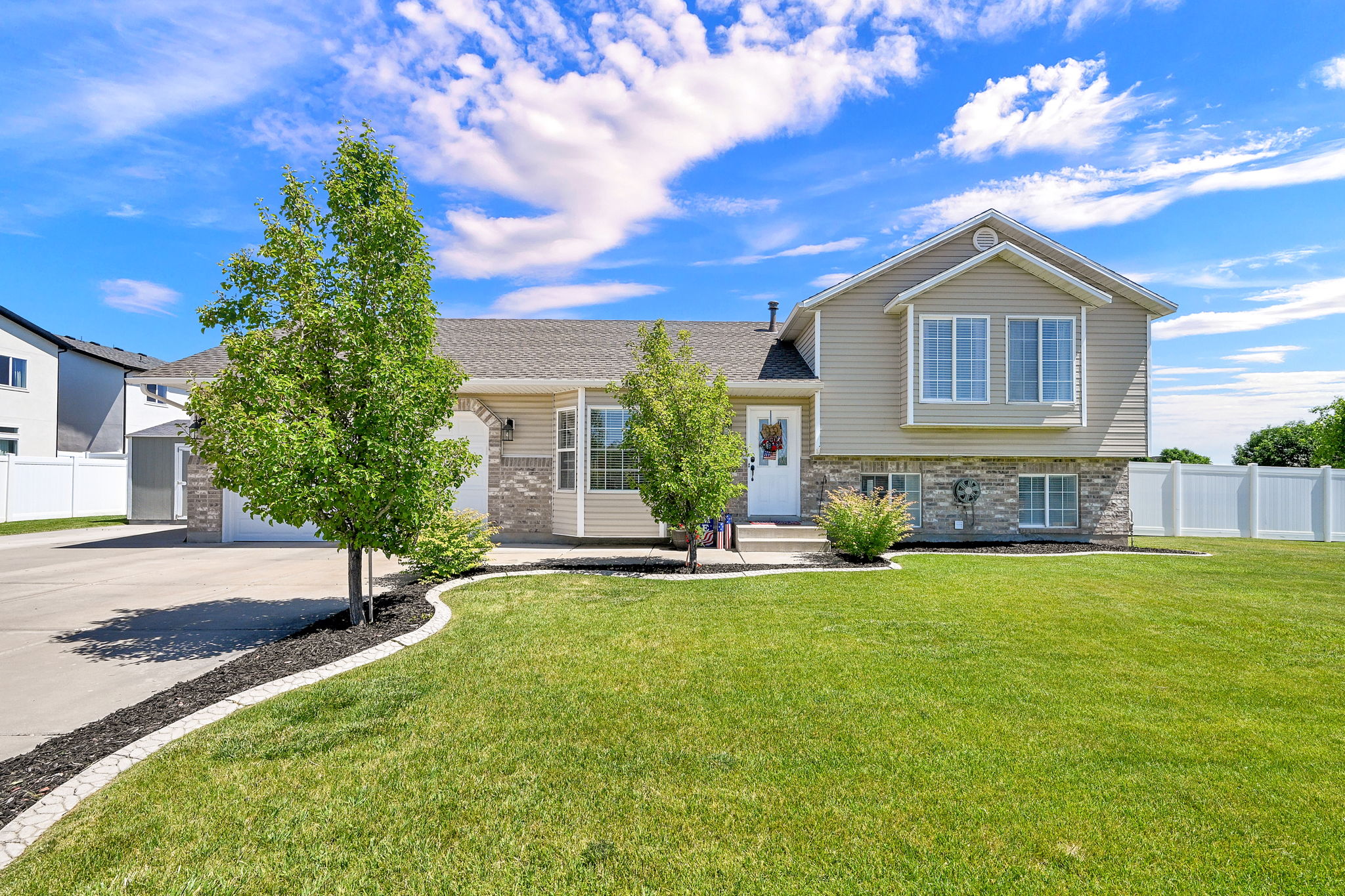 Split-level residence featuring a multi-pane bay window, beige siding, and stone veneer accents