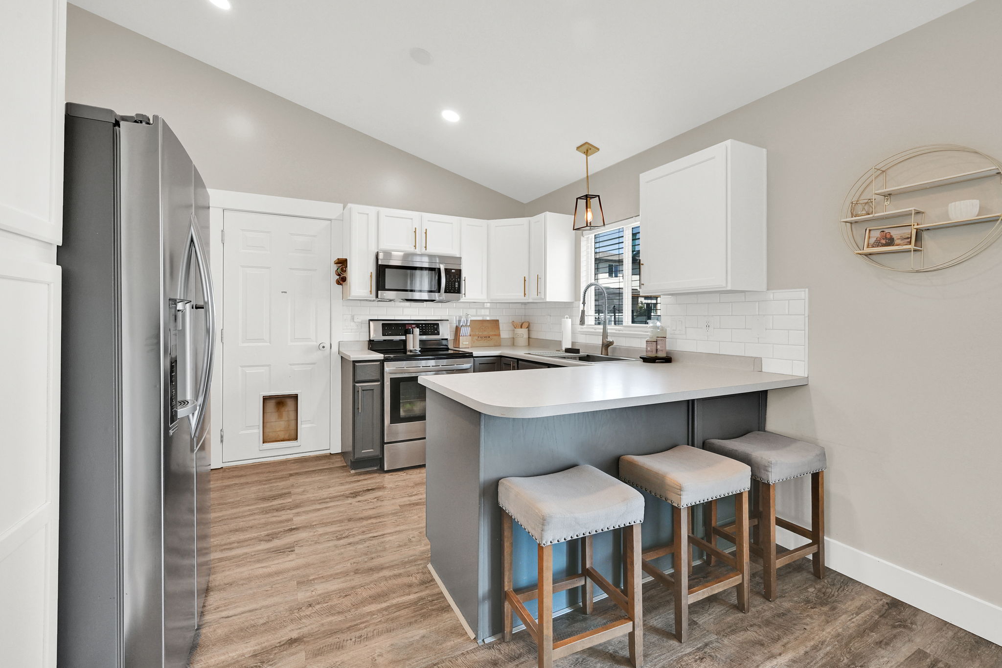 Kitchen featuring vaulted ceilings, wood-finish flooring, stainless steel appliances, white shaker cabinetry, and a subway tile backsplash