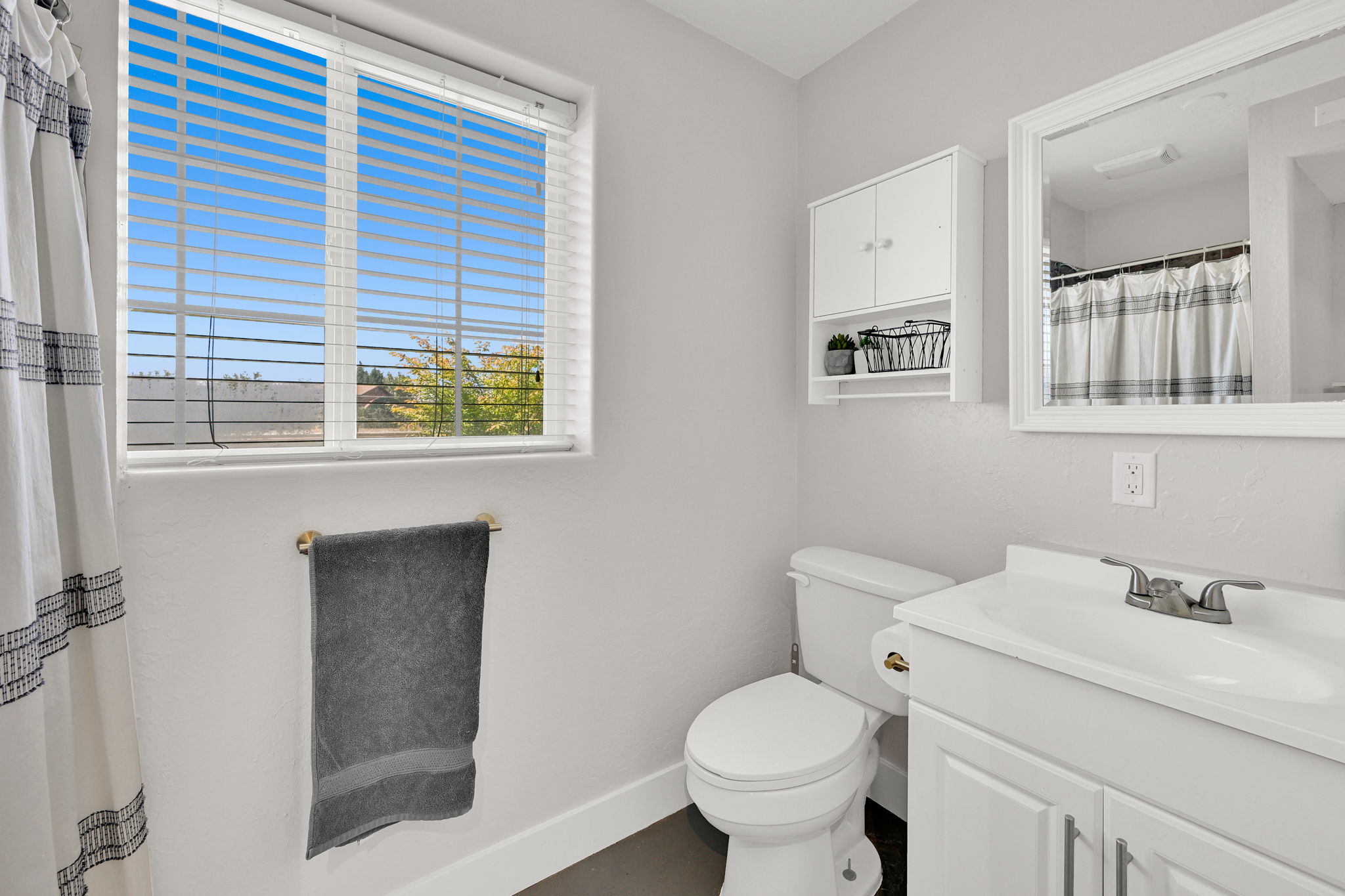 Bathroom featuring a window with blinds, a white vanity with an integrated sink, a wall-mounted medicine cabinet, and a framed mirror
