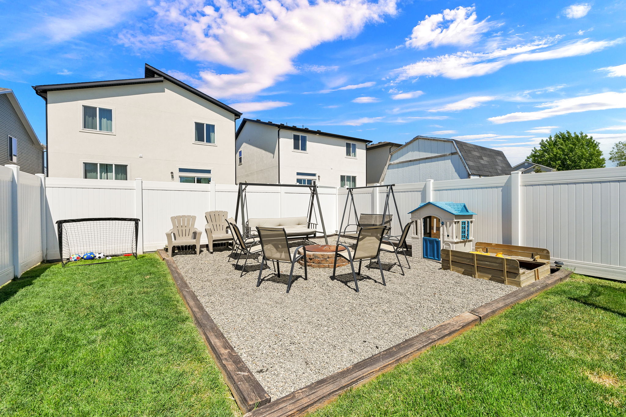 Fenced backyard featuring a gravel patio area with a fire pit, a separate grassy lawn, and white privacy fencing