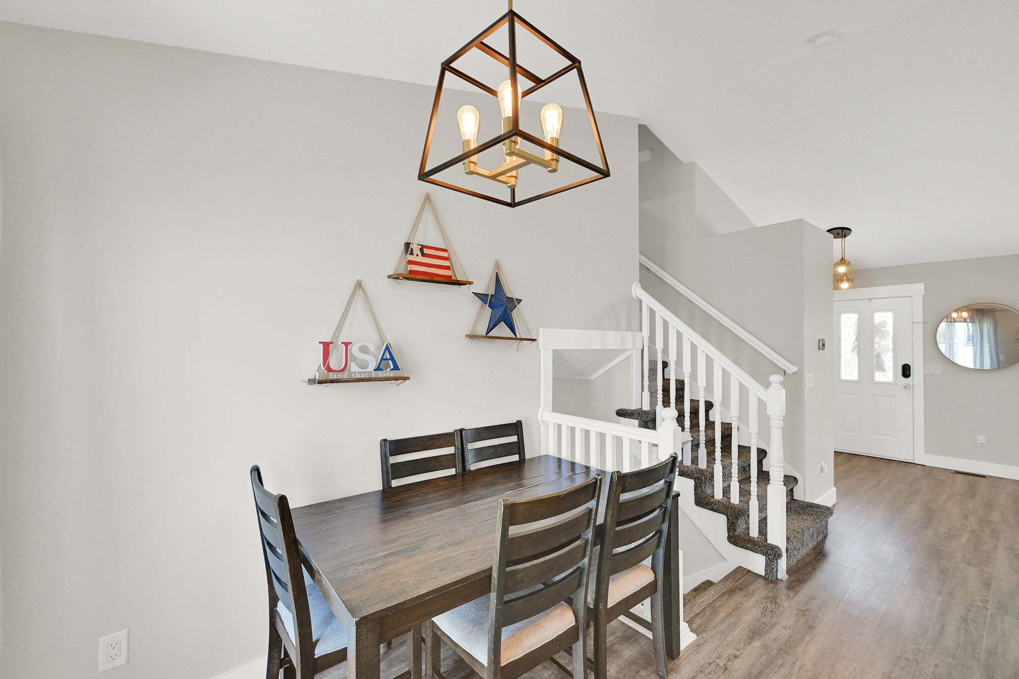Dining area featuring an open-cage chandelier with exposed bulbs, wood-finish flooring, and a staircase with white risers and carpeting