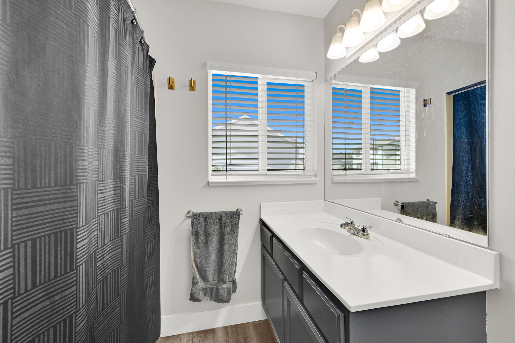 Bathroom featuring a white vanity countertop with an integrated sink, dual windows with blinds, a large wall-mounted mirror, and wood-finish flooring