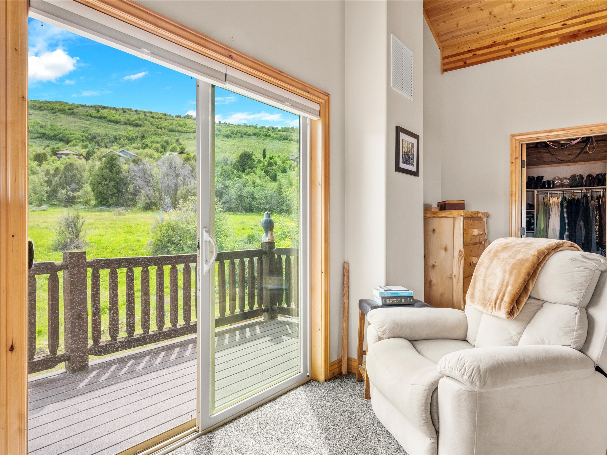 Sliding glass door opening to an outdoor deck with a natural wood railing, featuring a verdant hillside backdrop