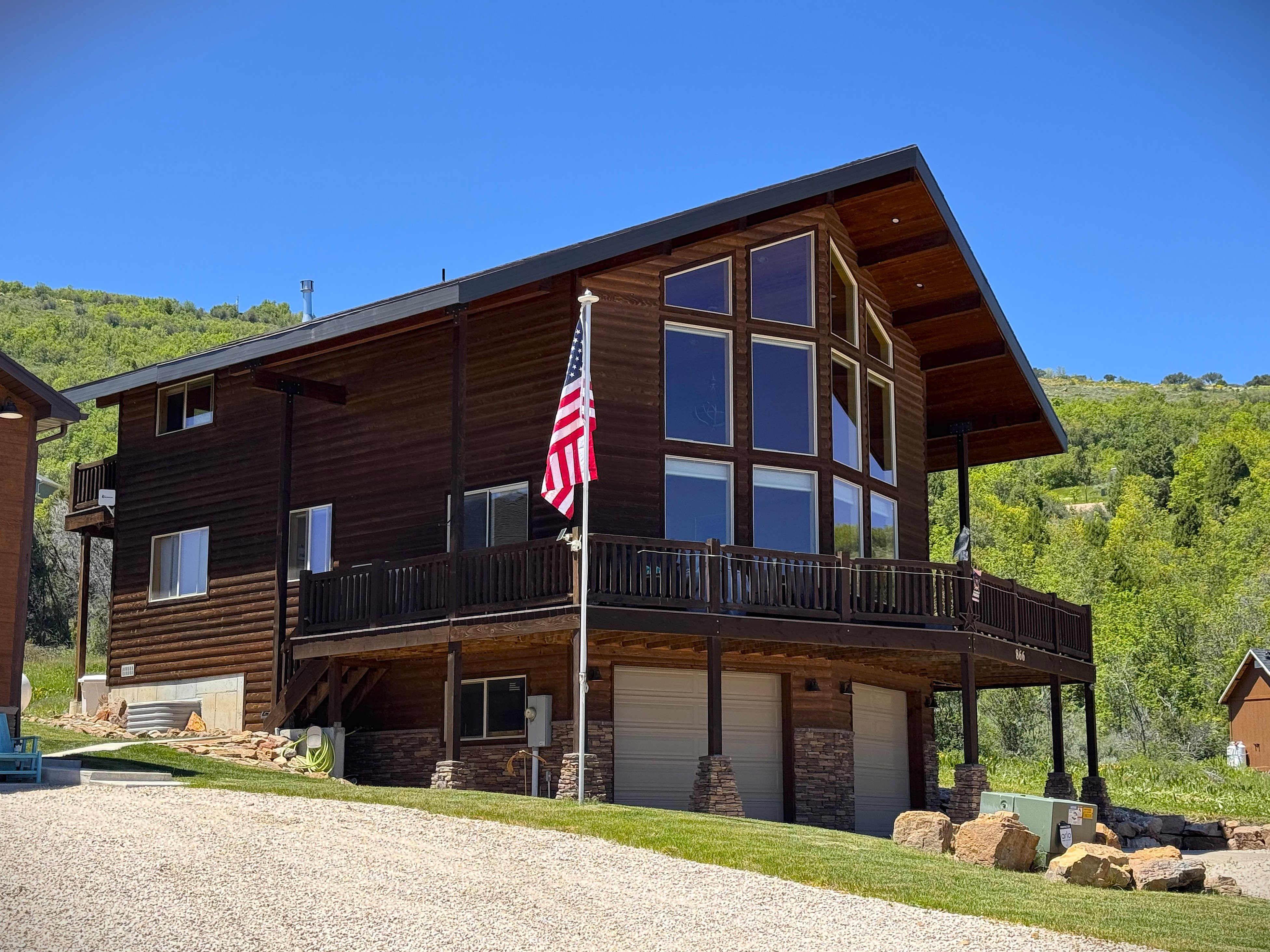 Two-story log-style home featuring an expansive front deck and a prominent  window wall