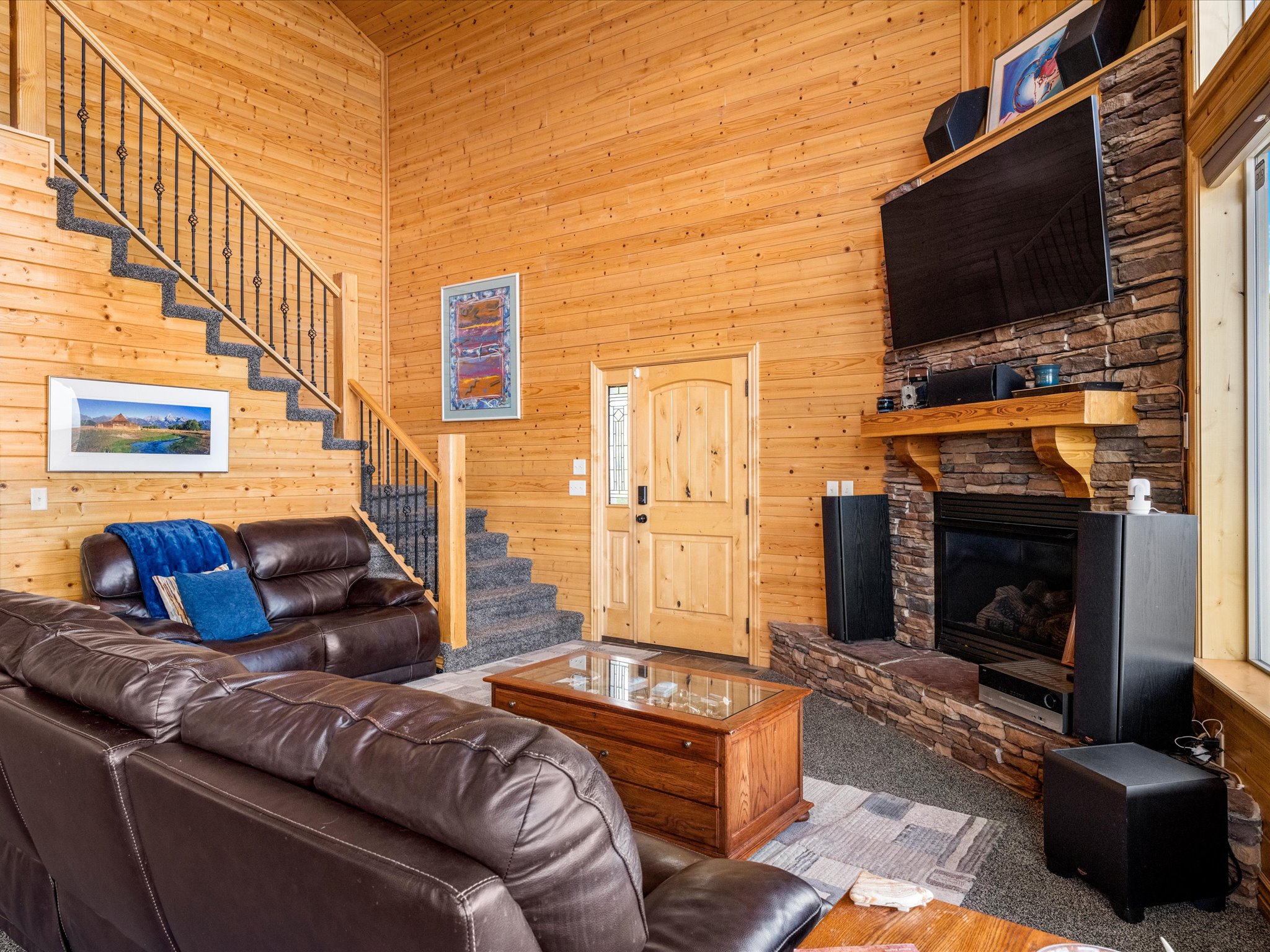 Living area featuring extensive wood paneling, a stone-faced fireplace with a wood mantel