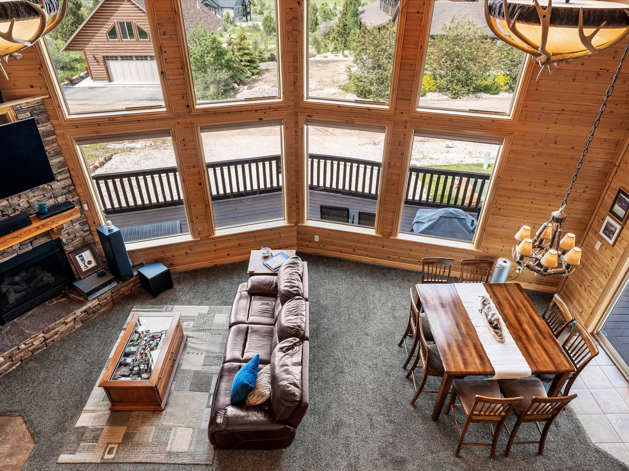 Vaulted ceilings with natural wood paneling, floor-to-ceiling windows, a stone-clad fireplace, and a dedicated dining area featuring a wood table and chairs