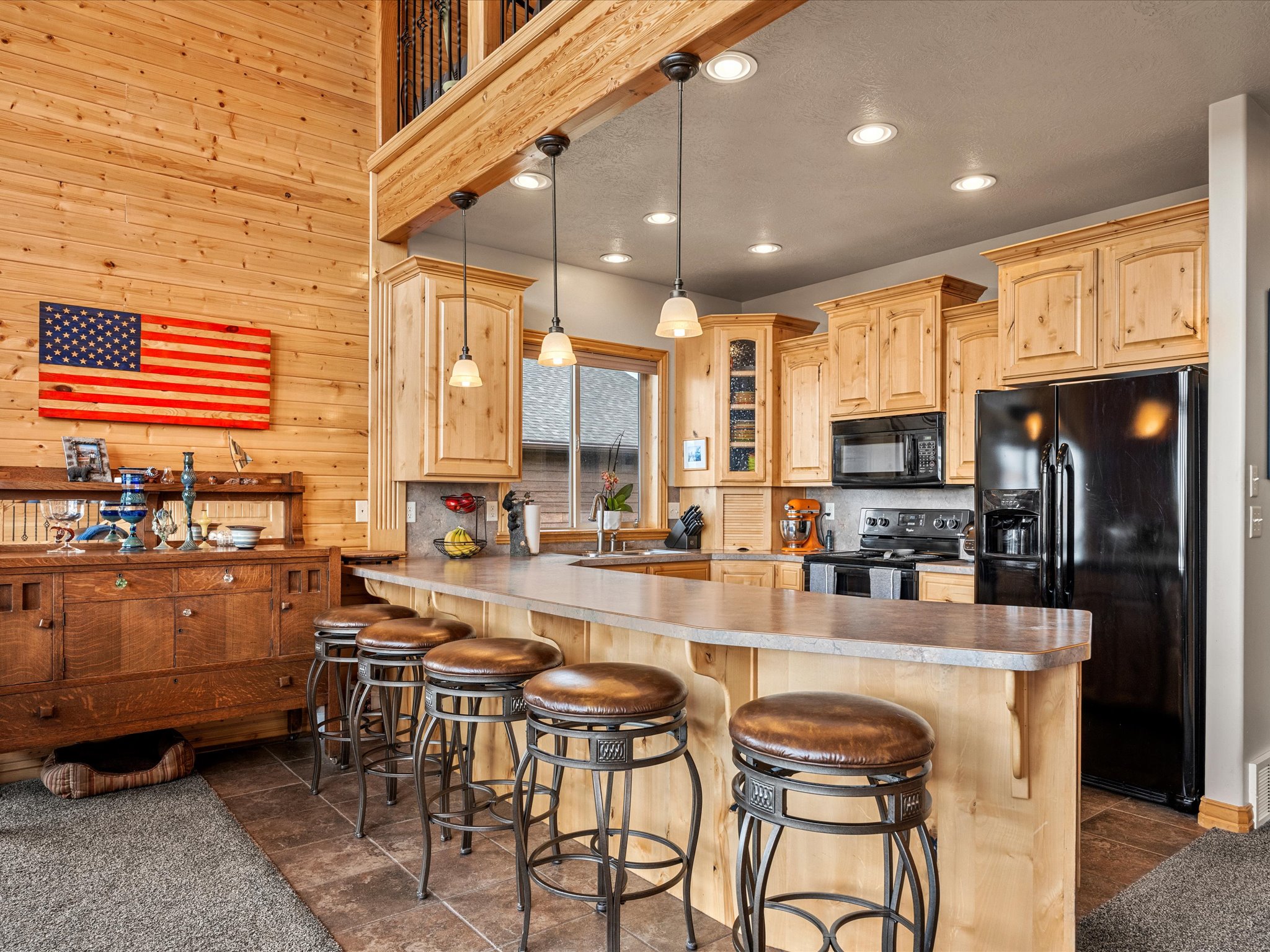Open-concept kitchen featuring light wood-finish cabinetry, black appliances, a peninsula with bar seating, and recessed lighting
