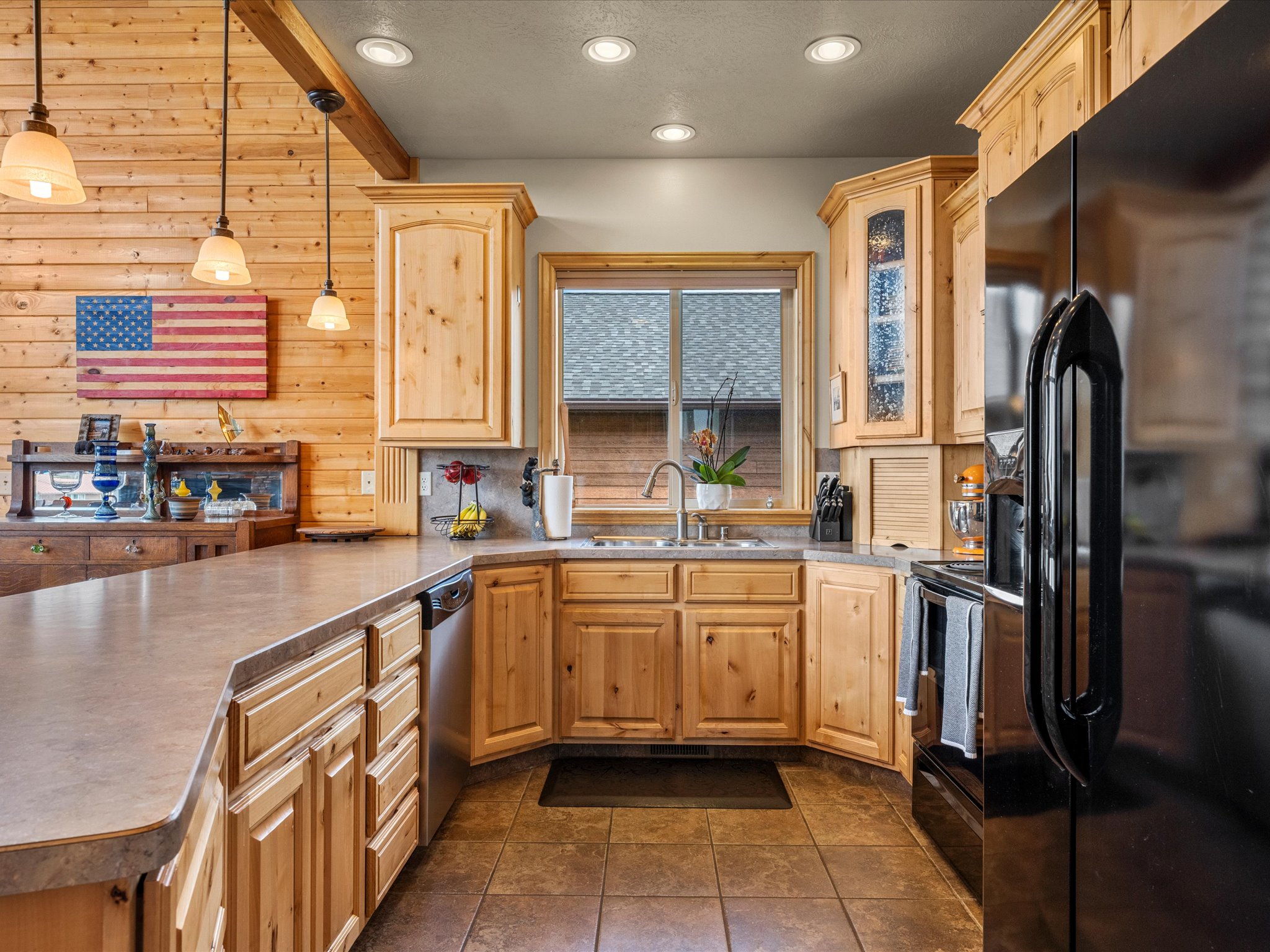 Kitchen featuring light wood cabinetry, a built-in stainless steel dishwasher, and a black refrigerator