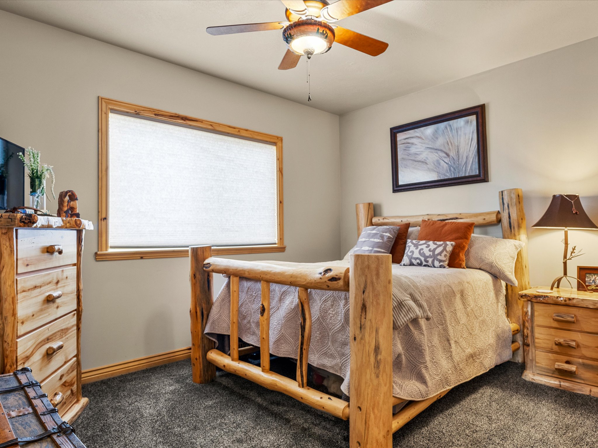 Bedroom featuring a wood-trimmed window with roller shade, neutral wall paint, and carpet flooring