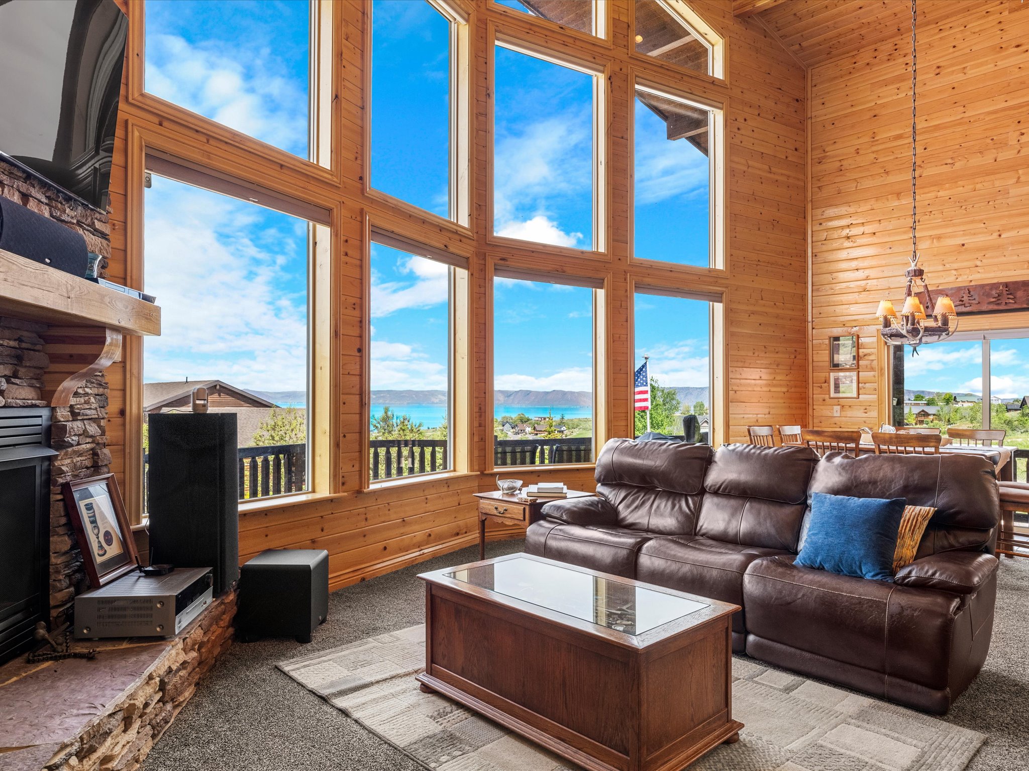 Two-story living area featuring extensive natural wood paneling, a stone-clad fireplace, and multiple floor-to-ceiling windows with expansive water and landscape views