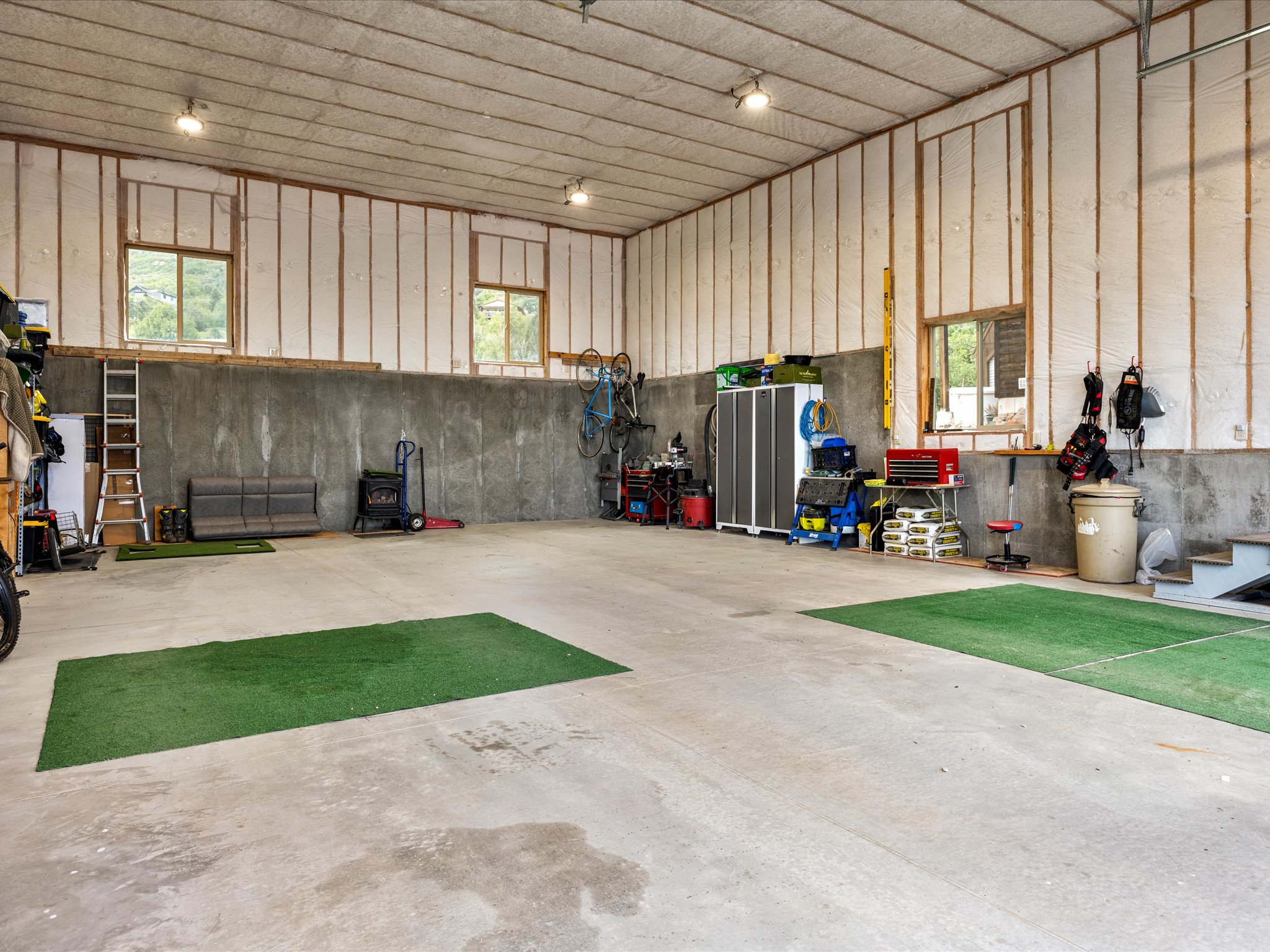 Spacious garage featuring a concrete floor, two windows providing natural light, exposed wood framing with insulation, and track lighting fixtures
