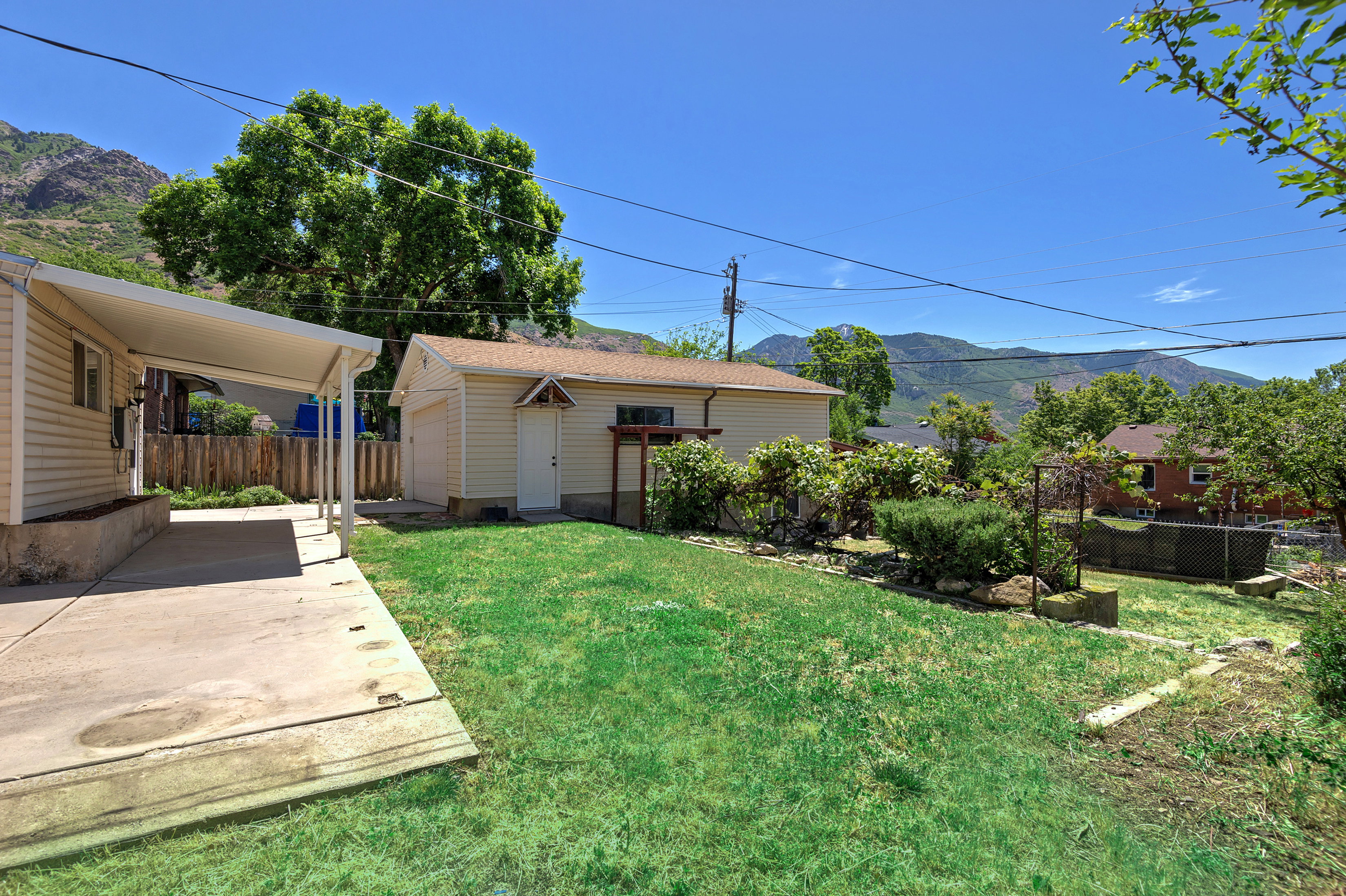 Expansive backyard featuring a concrete patio, covered carport, detached garage, and mountain backdrop