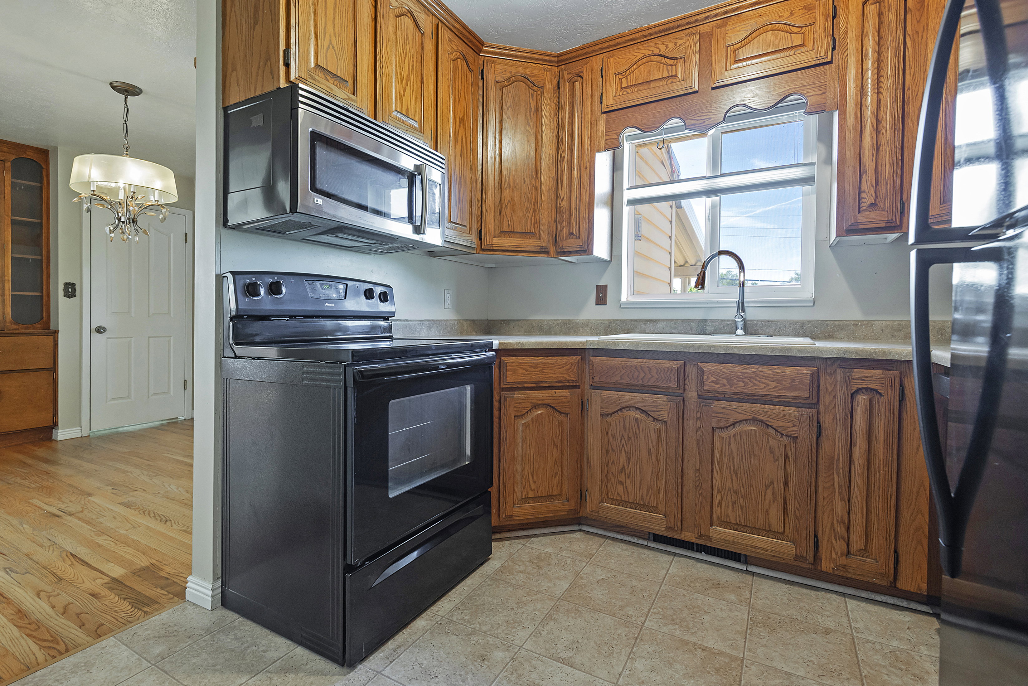 Kitchen featuring wood cabinetry, stainless steel microwave, black electric range, and a window above the sink