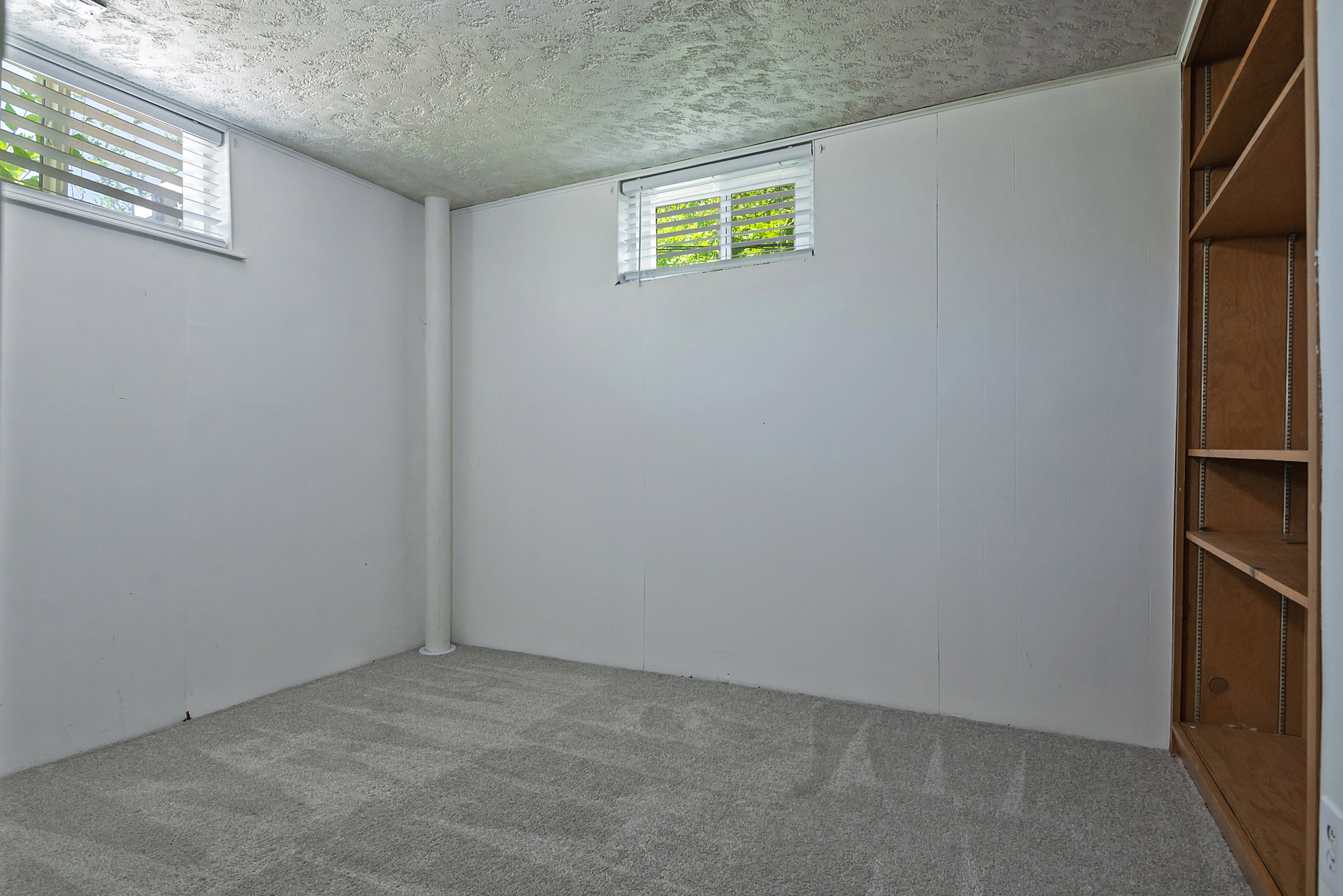 Carpeted room featuring two windows with blinds and a built-in wooden shelving unit