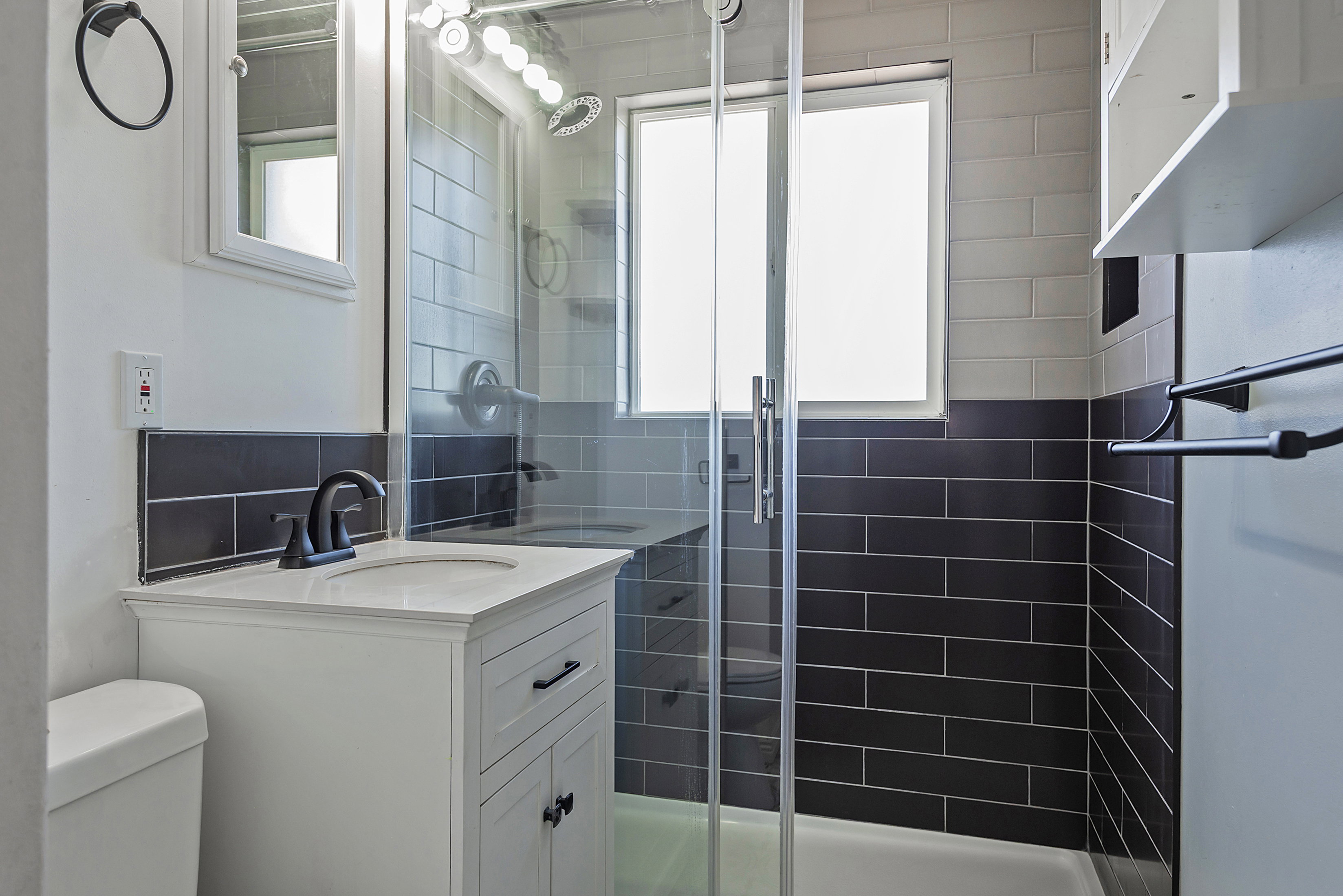 Bathroom featuring a glass-enclosed shower, two-tone subway tile, a vanity with integrated sink, matte black fixtures, and a wall-mounted medicine cabinet