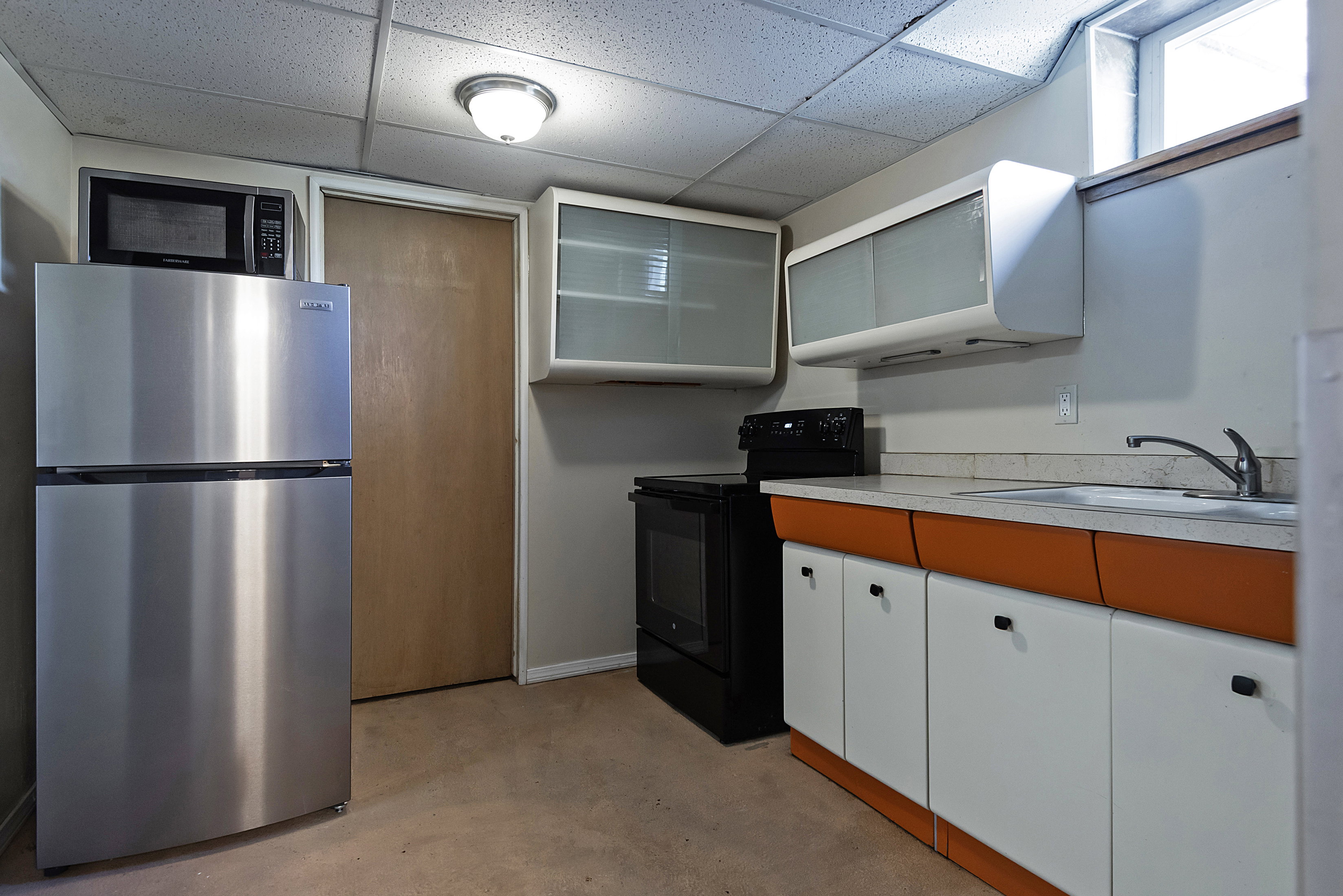 Compact kitchen featuring a stainless steel refrigerator, black electric range, and white cabinetry with orange accents